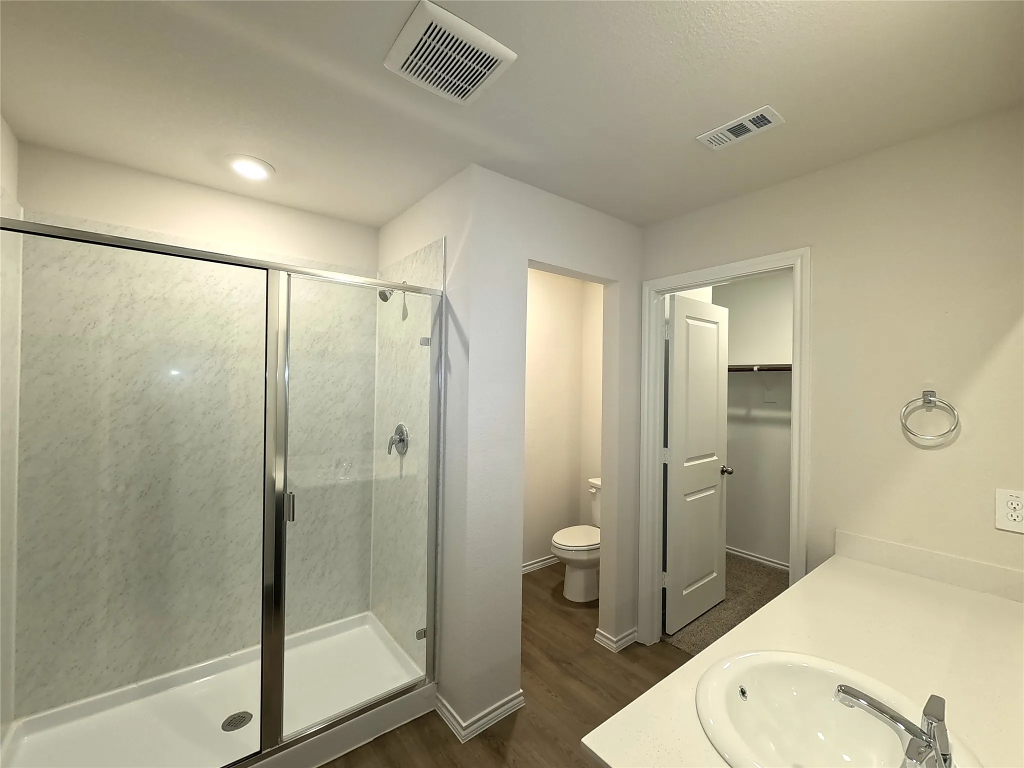 Walk-in shower with a glass enclosure, solid-surface countertop with an integrated sink, wood-finish flooring, and a separate water closet area
