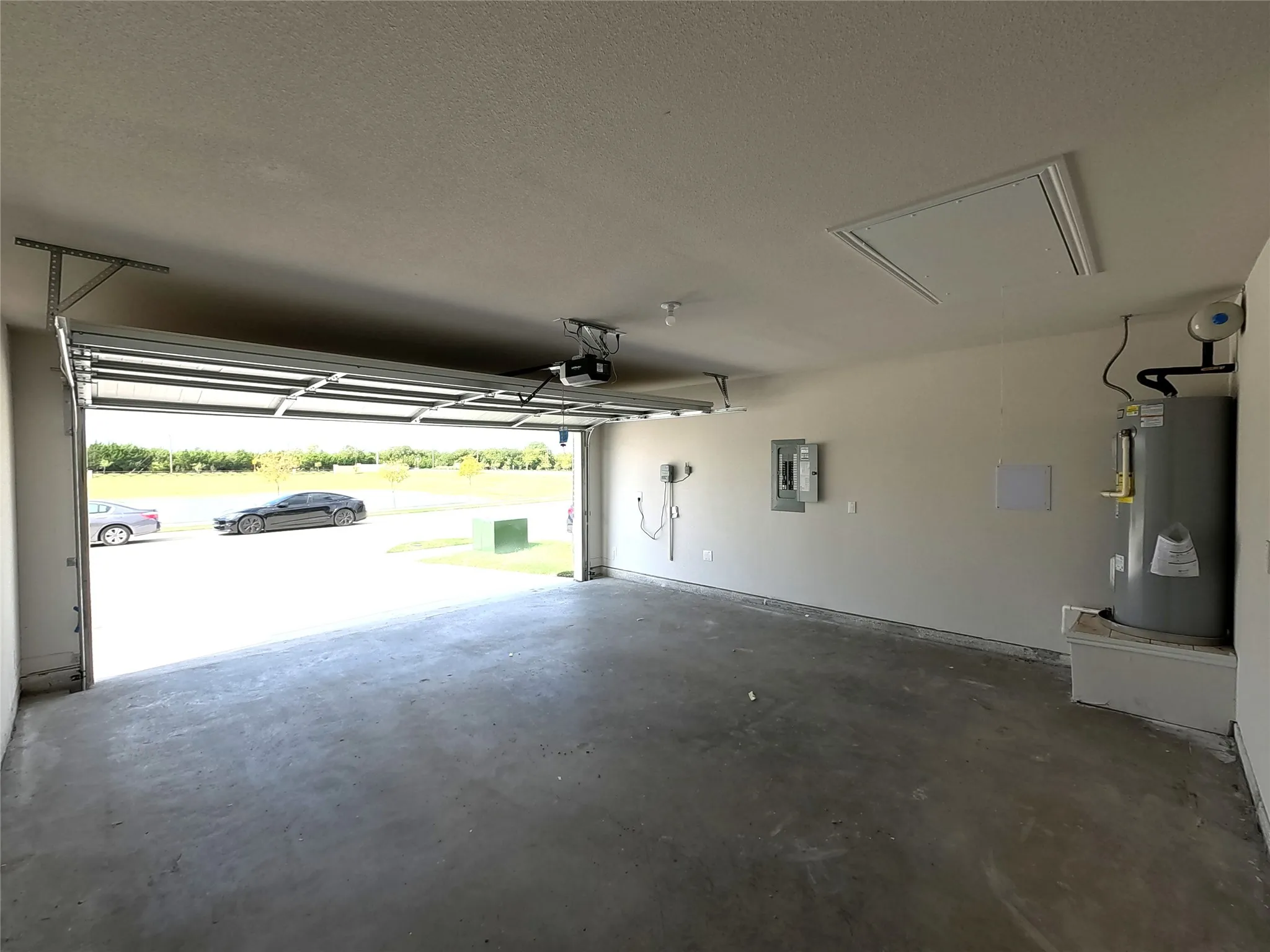 Attached two-car garage featuring a concrete floor, automated overhead door, electrical panel, and elevated water heater platform