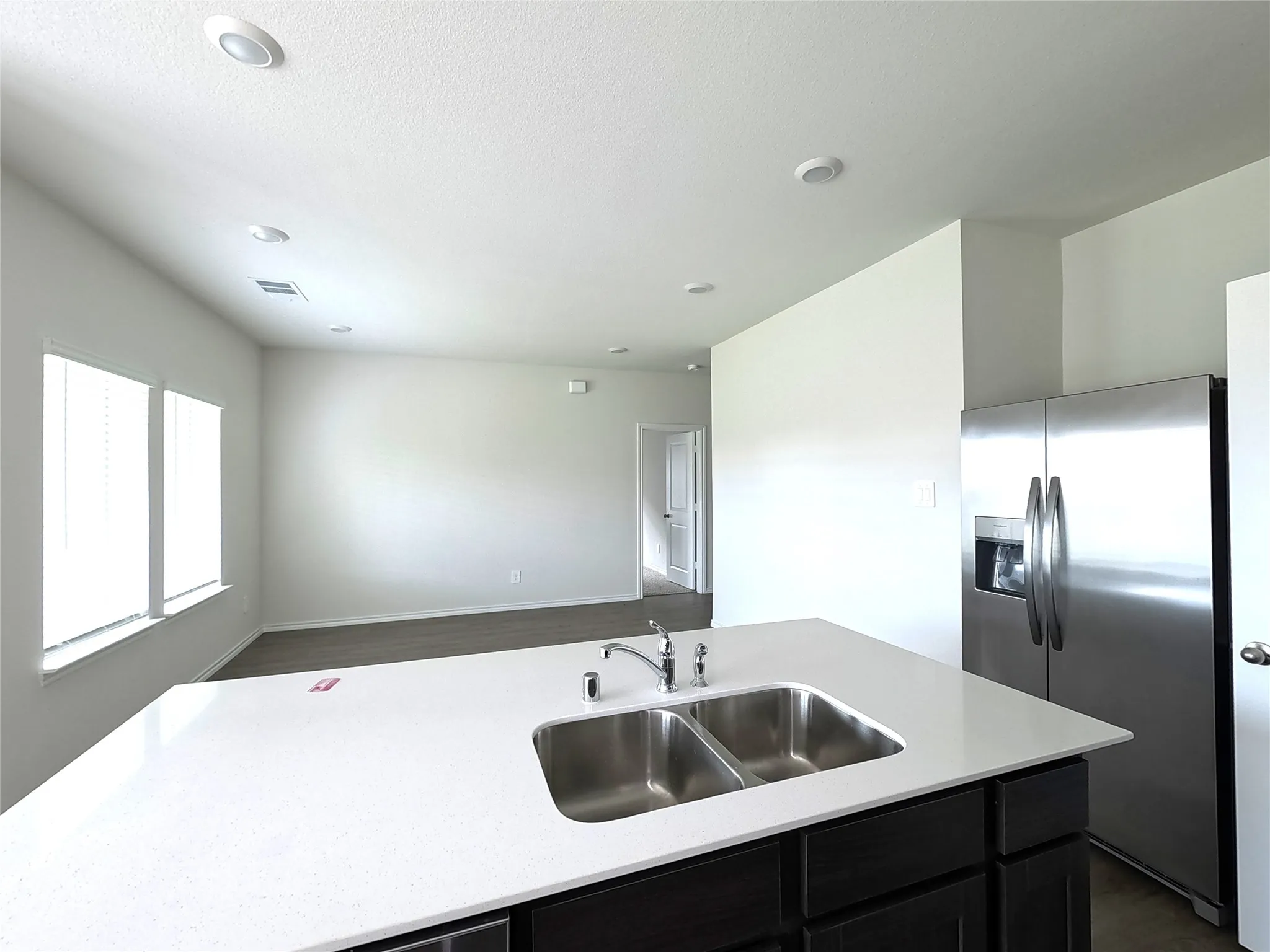Kitchen island featuring a dual-basin stainless steel sink, polished chrome faucet, and solid-surface countertop, complemented by dark-toned cabinetry and a stainless steel refrigerator