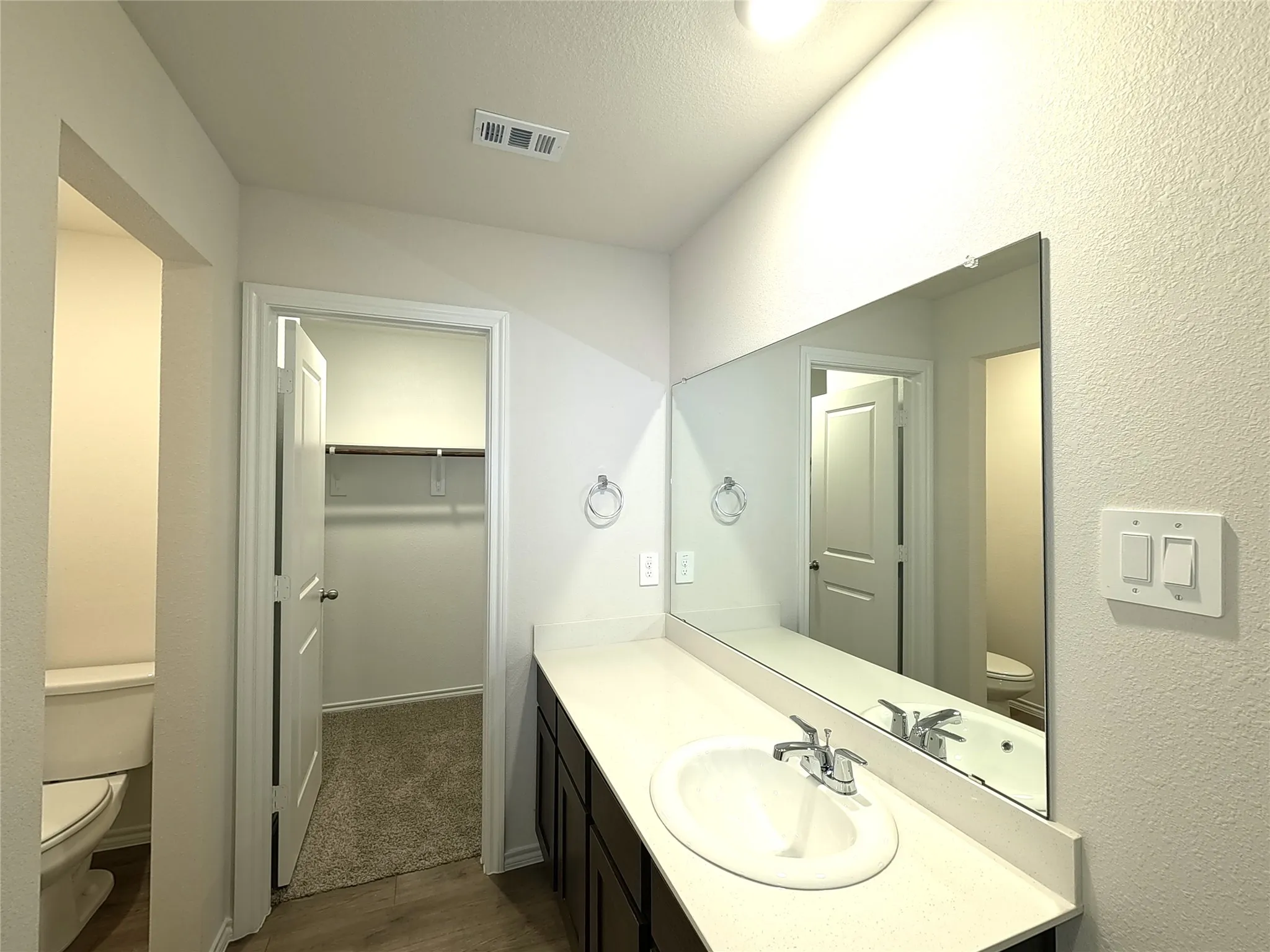 Bathroom vanity featuring dark-finished cabinetry, solid-surface countertop, integrated oval basin, and a full-width wall mirror