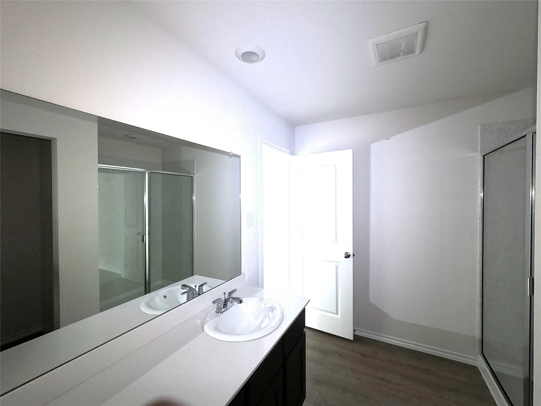 Bathroom featuring a white vanity with a composite countertop, undermount sink, chrome faucet, expansive wall mirror, and a glass-enclosed shower