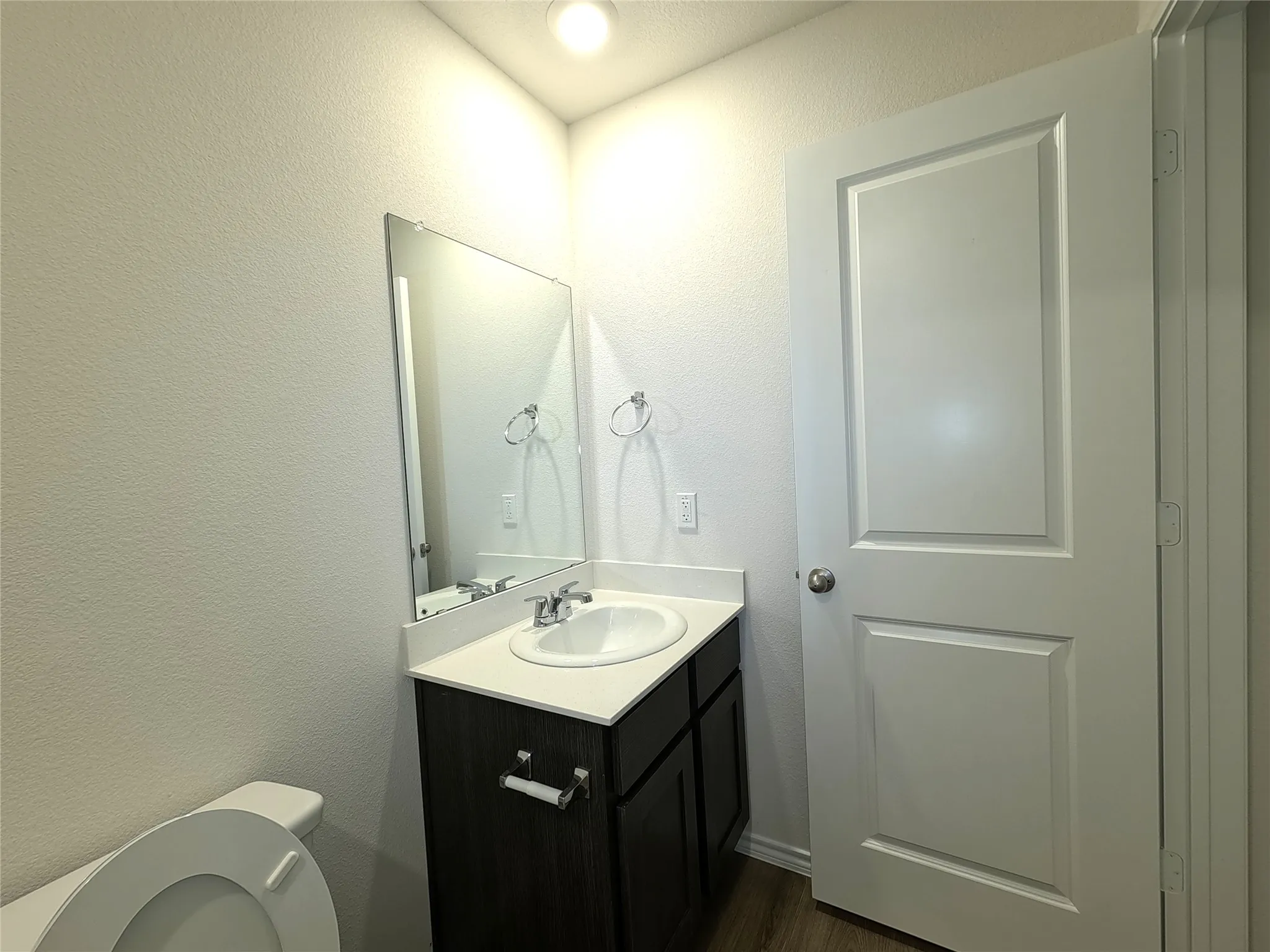 Single-sink vanity featuring a dark-finish cabinet, integrated countertop with oval basin, wall-mounted mirror, and brushed-metal fixtures