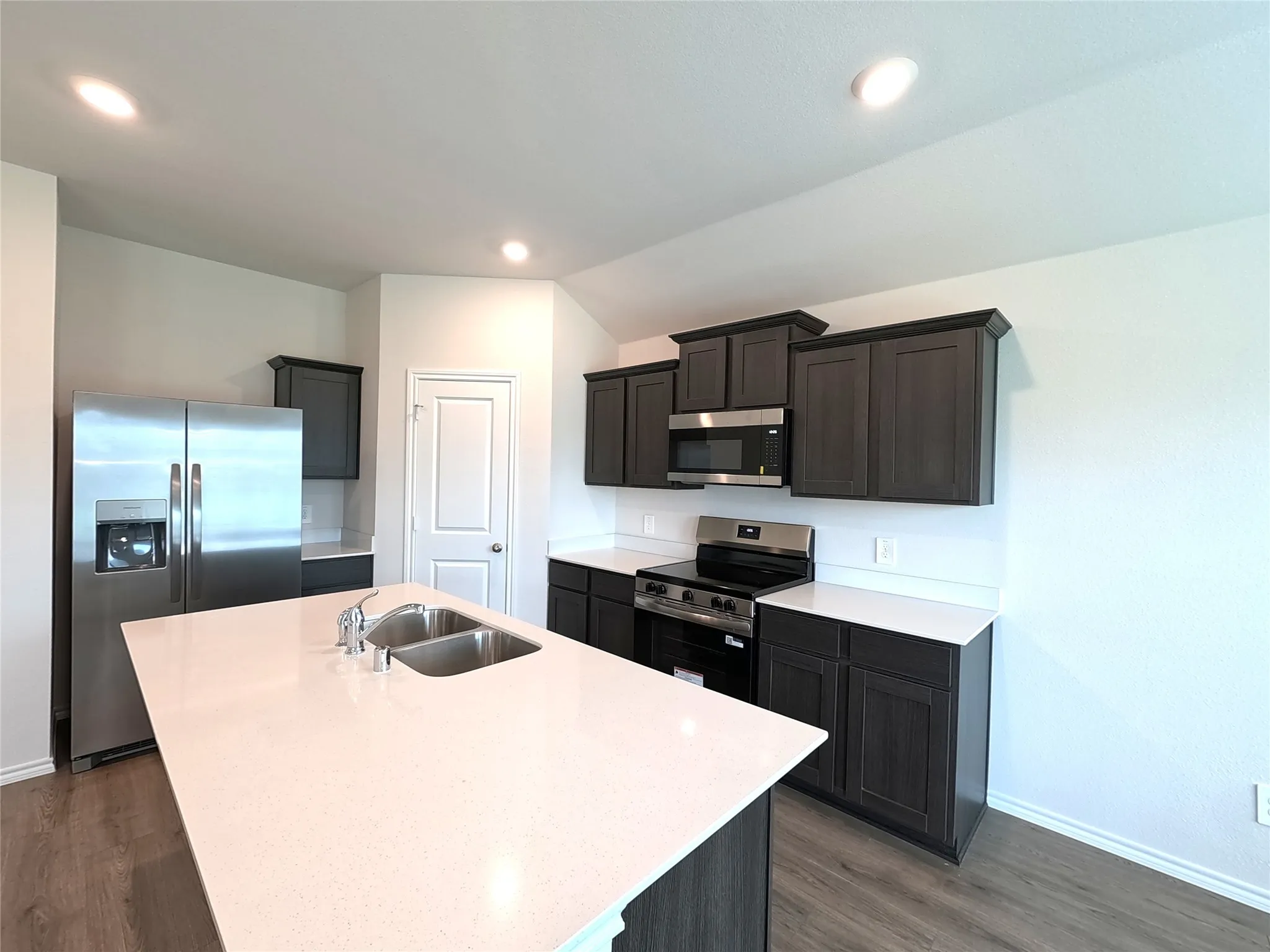 Kitchen featuring dark cabinetry, solid-surface countertops, center island with an undermount double-basin sink, and stainless steel appliances