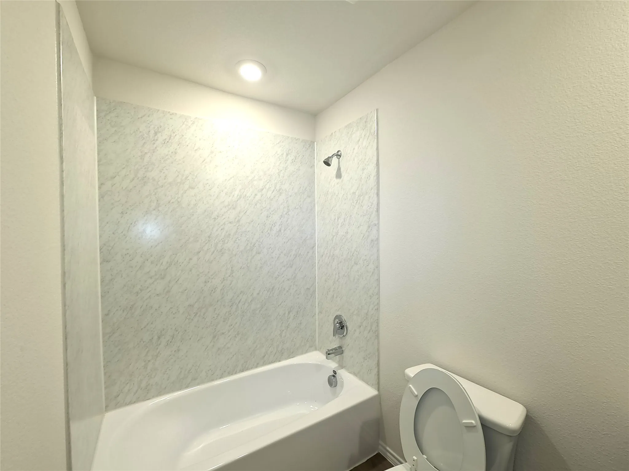Bathroom featuring a white soaking tub with stone-patterned wall surround, polished chrome shower head and faucet hardware, and recessed ceiling lighting