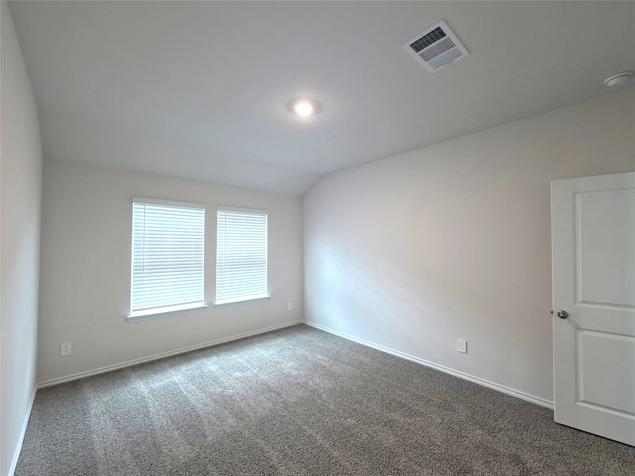 Room featuring neutral wall tones, plush carpeting, a vaulted ceiling, and dual windows with integrated blinds