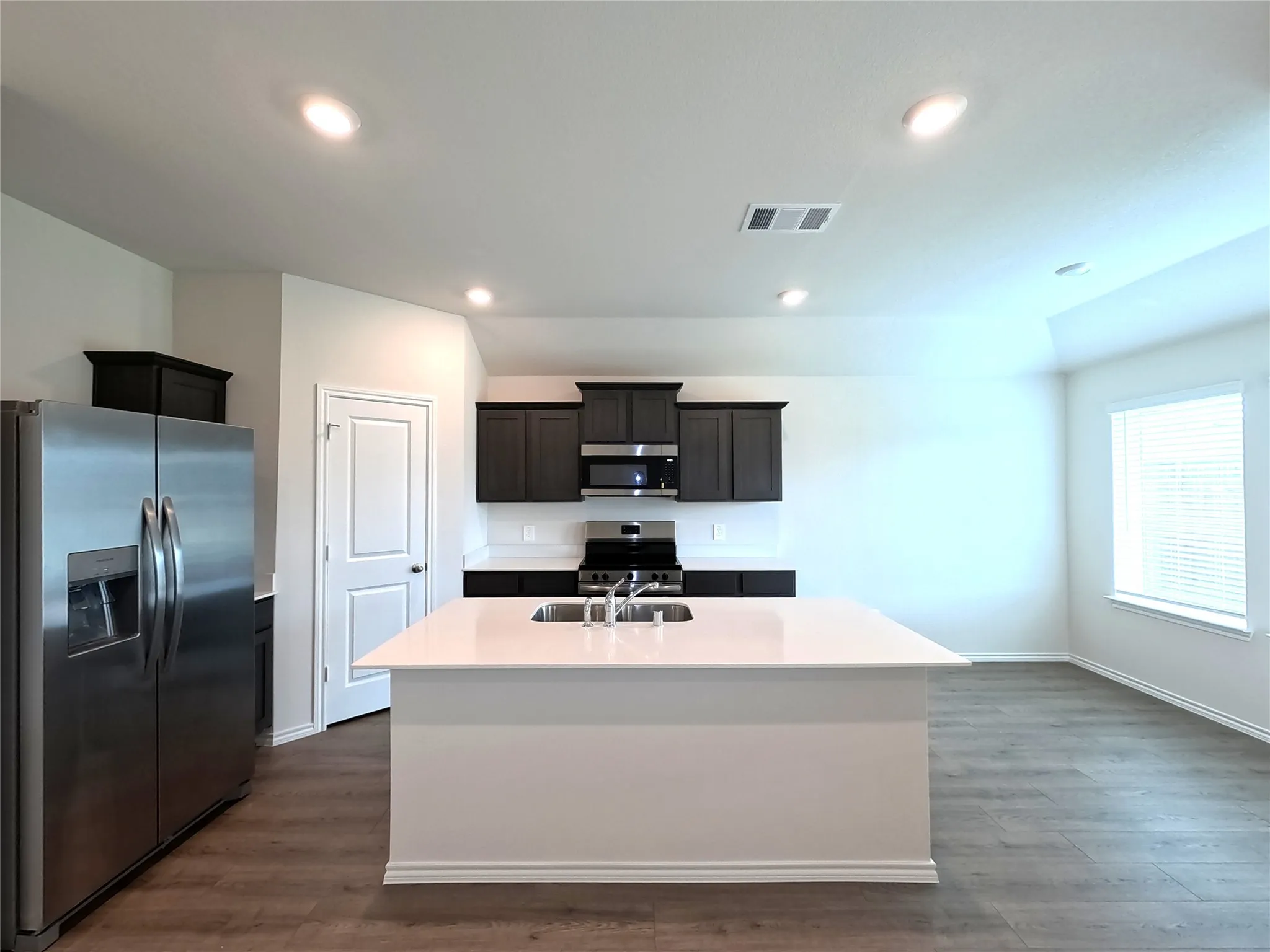 Kitchen featuring a center island with a solid surface countertop, dark cabinetry, stainless steel appliances, and wood-finish flooring