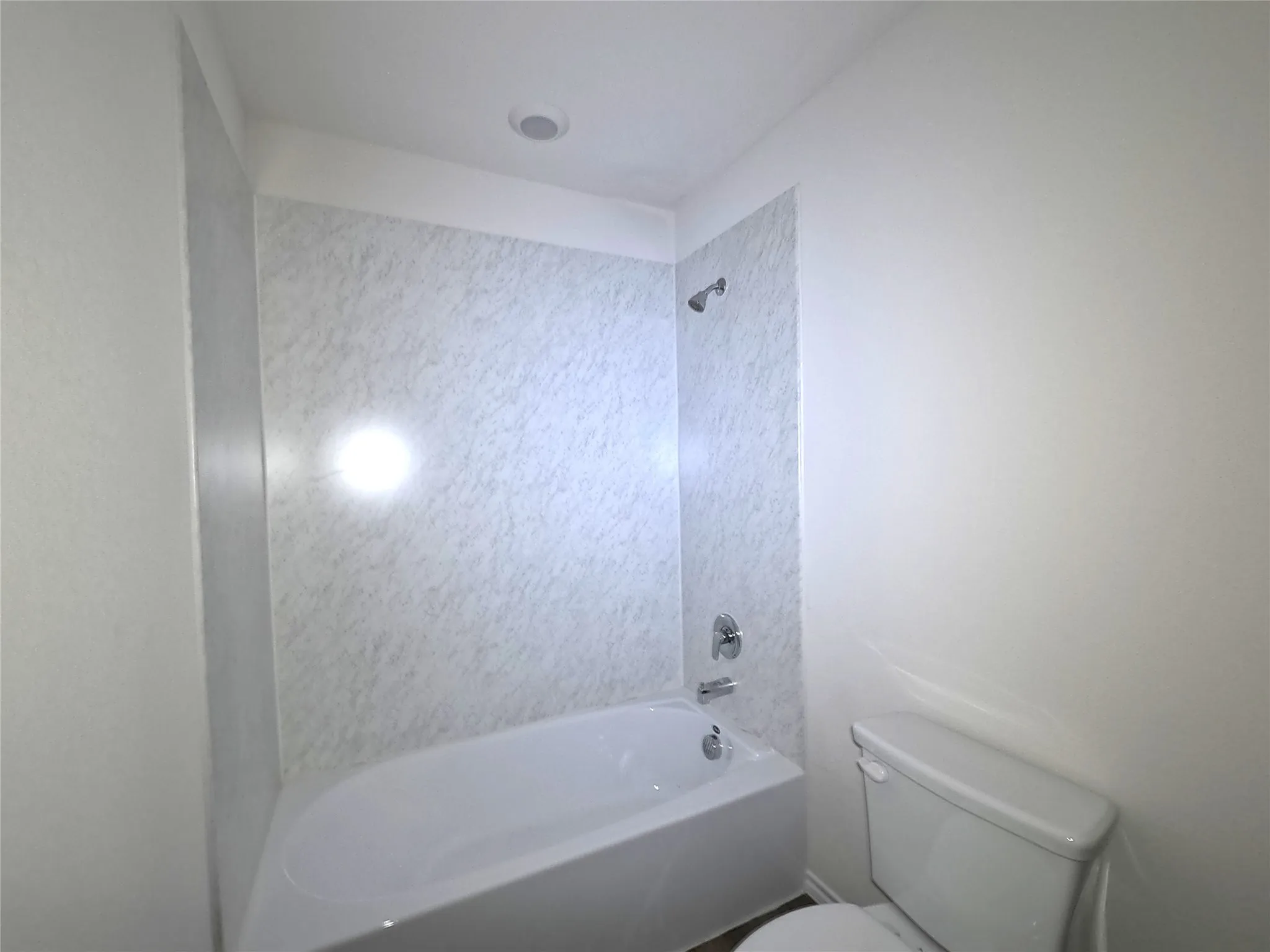 Bathtub with white surround featuring a marble-patterned finish, chrome shower head, and chrome faucet hardware