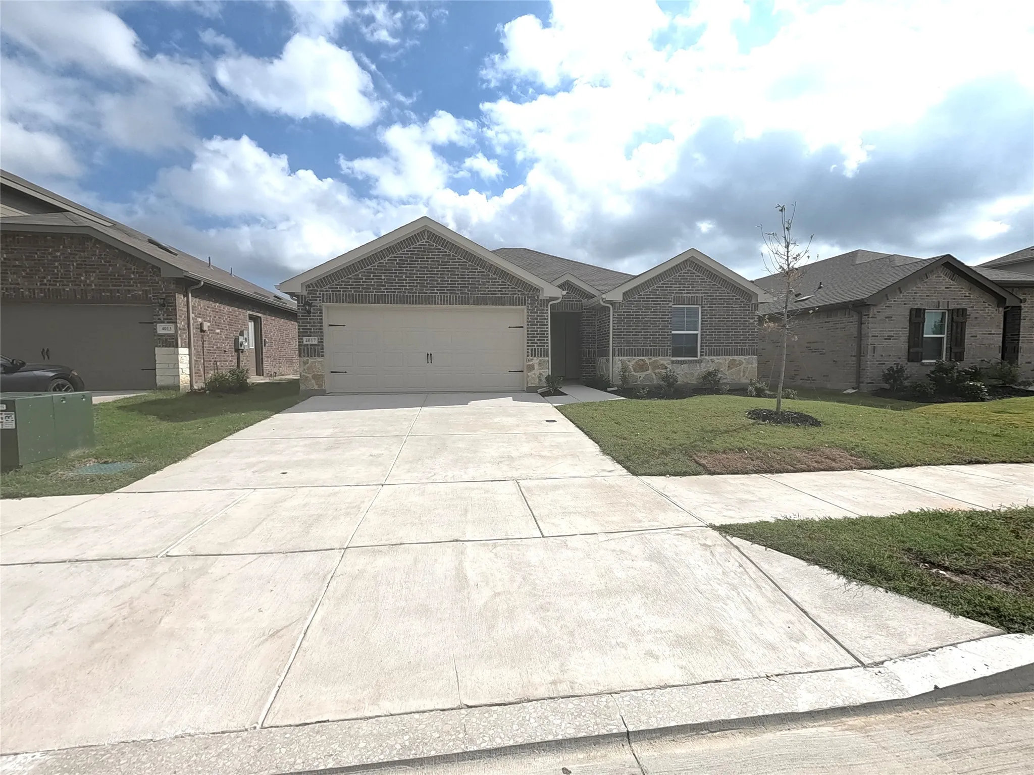 Single-story exterior featuring a brick and stone facade, dual-gabled roofline, two-car garage, and concrete driveway