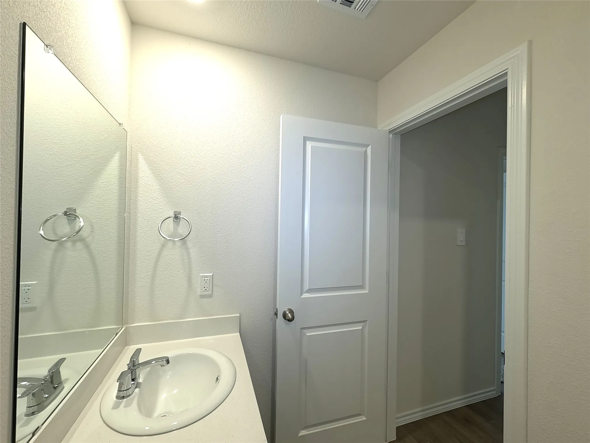 Vanity featuring an oval drop-in sink, solid-surface countertop, full-width wall mirror, and chrome dual-handle faucet