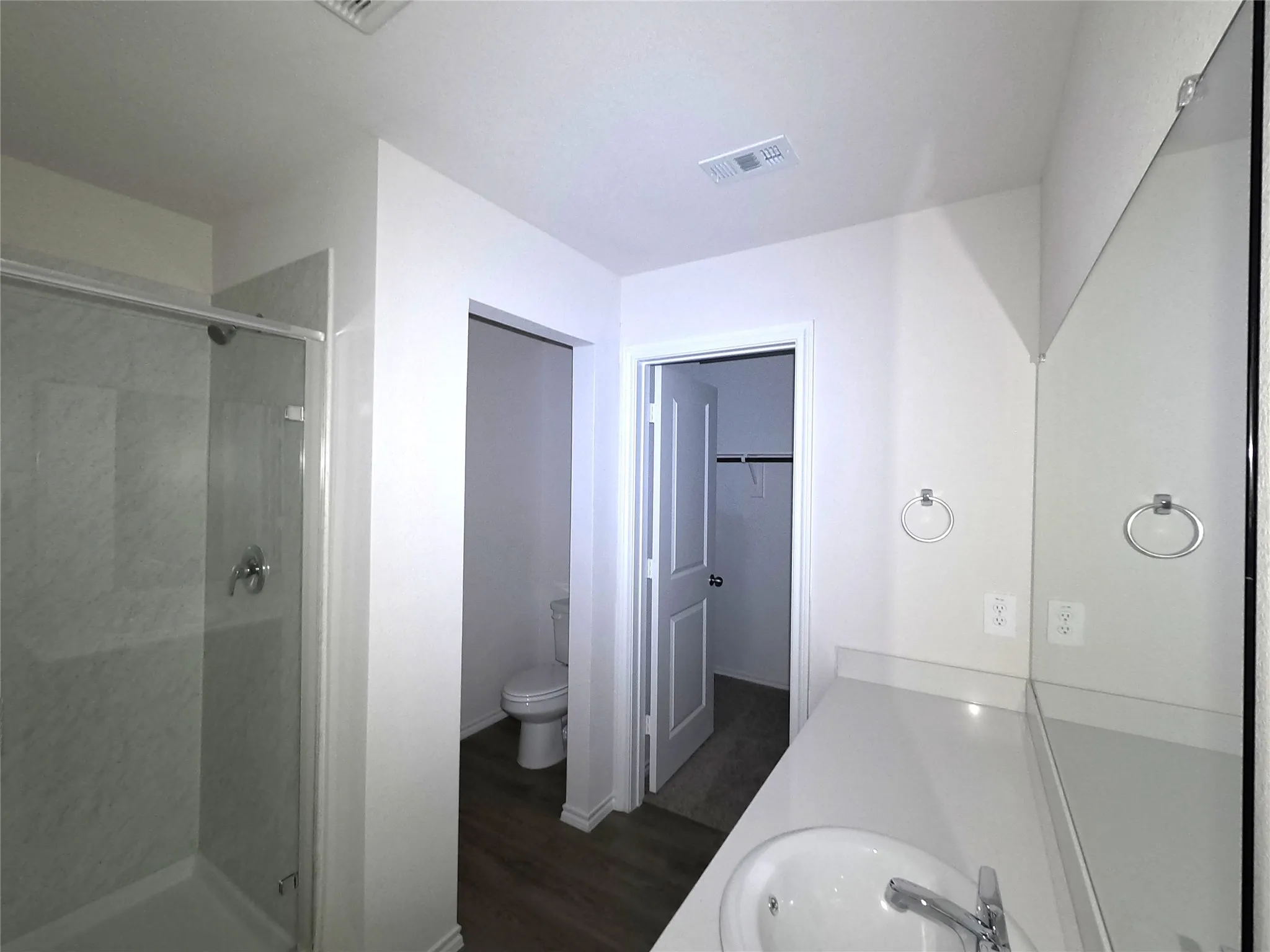 Full-width wall mirror, shower with glass enclosure and surround, solid-surface countertop with integrated basin, and neutral-tone flooring