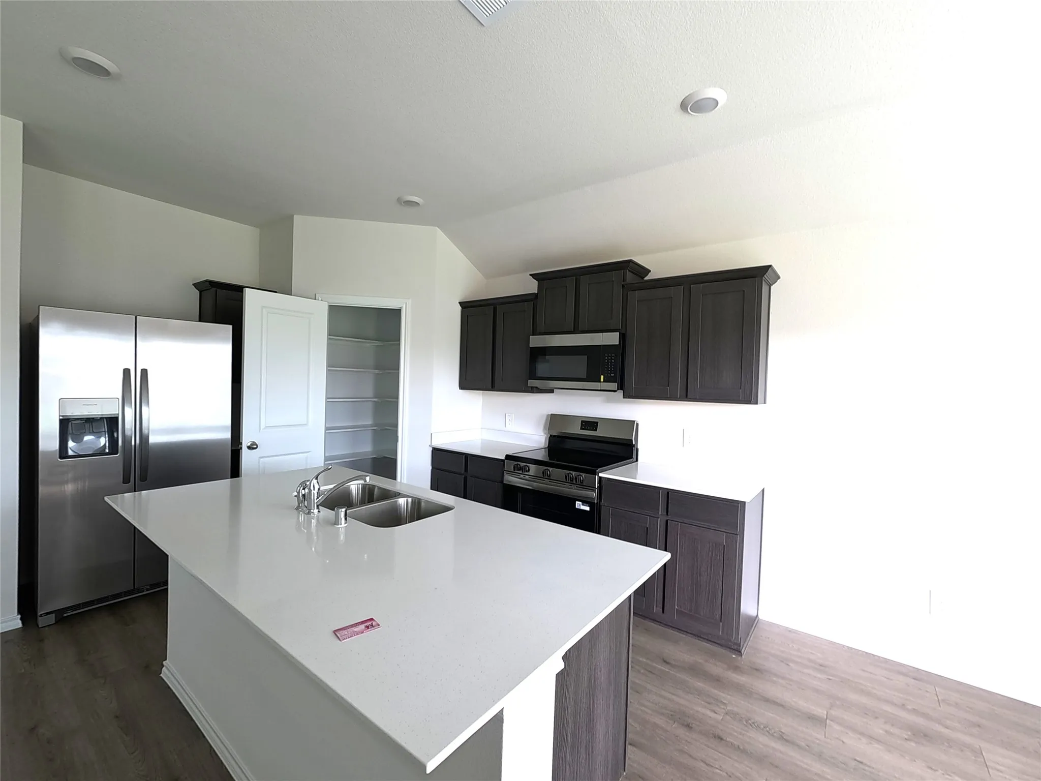 Kitchen featuring dark wood-finish cabinetry, quartz countertops, a central island with a double-basin stainless steel sink, stainless steel appliances, and a walk-in pantry