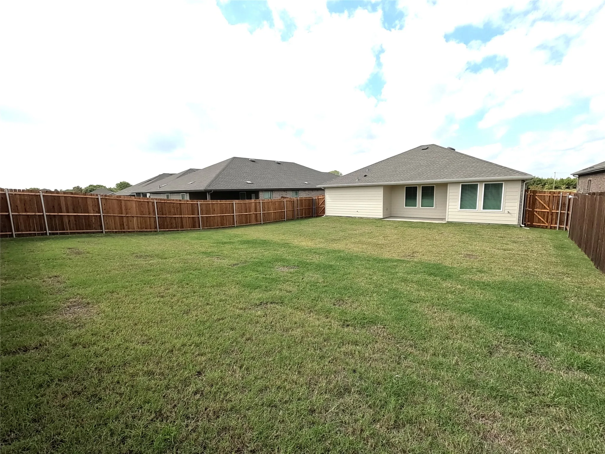 Expansive backyard featuring a large grass lawn, perimeter wood fencing, and a concrete patio slab