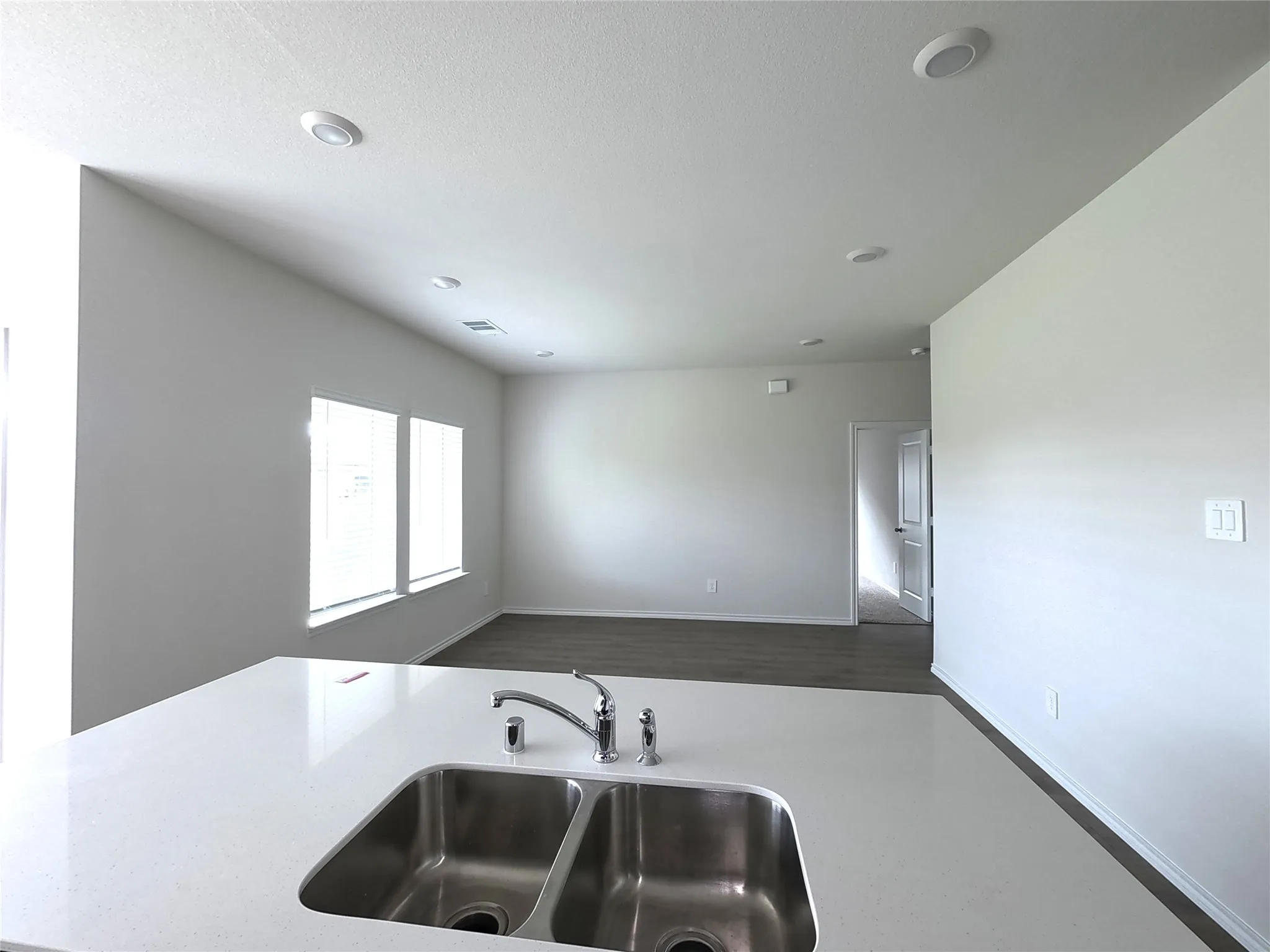 Solid surface countertop with a stainless steel double-basin undermount sink, high-arc faucet, recessed lighting, and wood-finish flooring