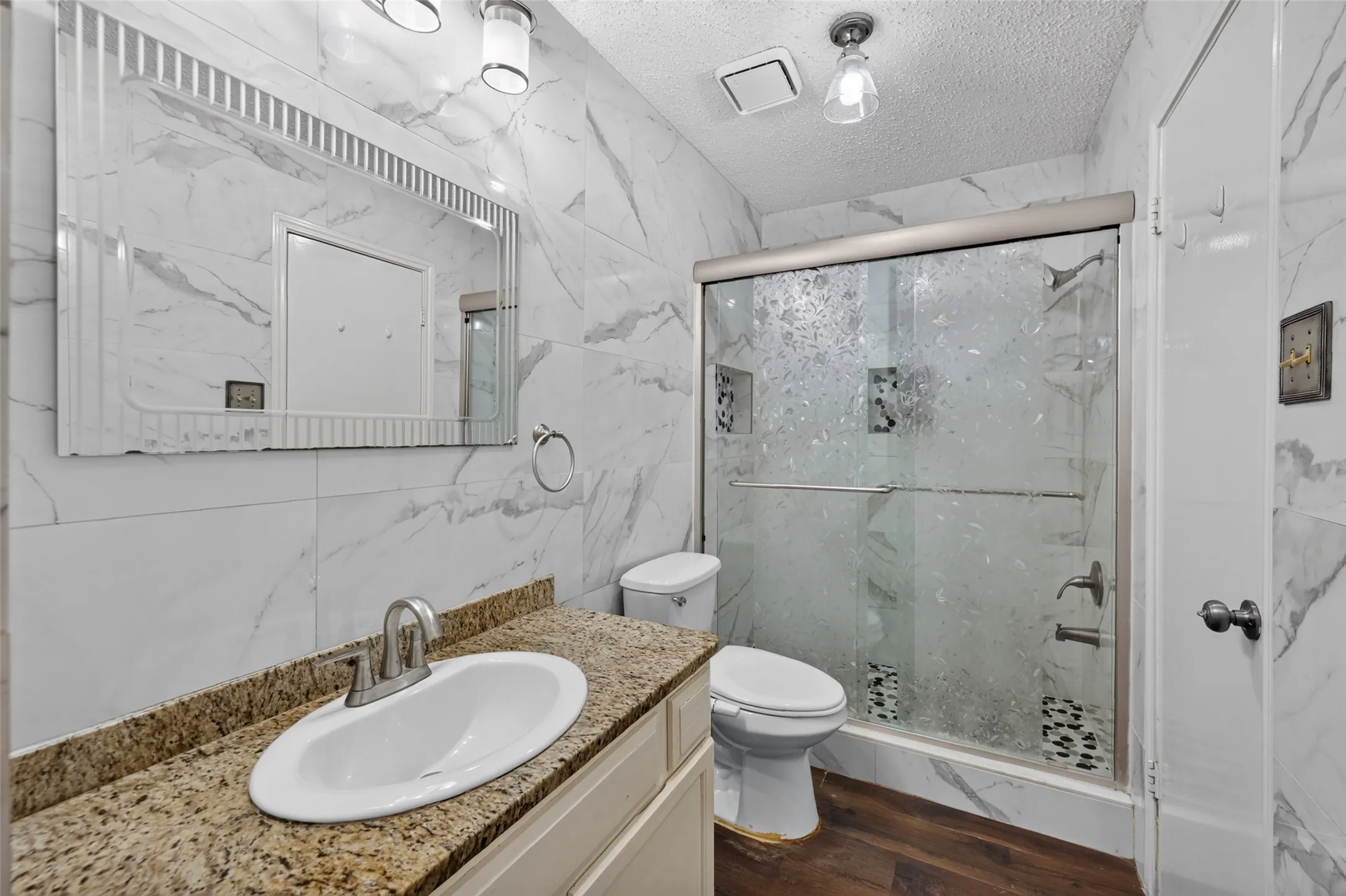 Full bathroom featuring a shower with a sliding glass door, a vanity with a granite countertop, and wood-finish flooring