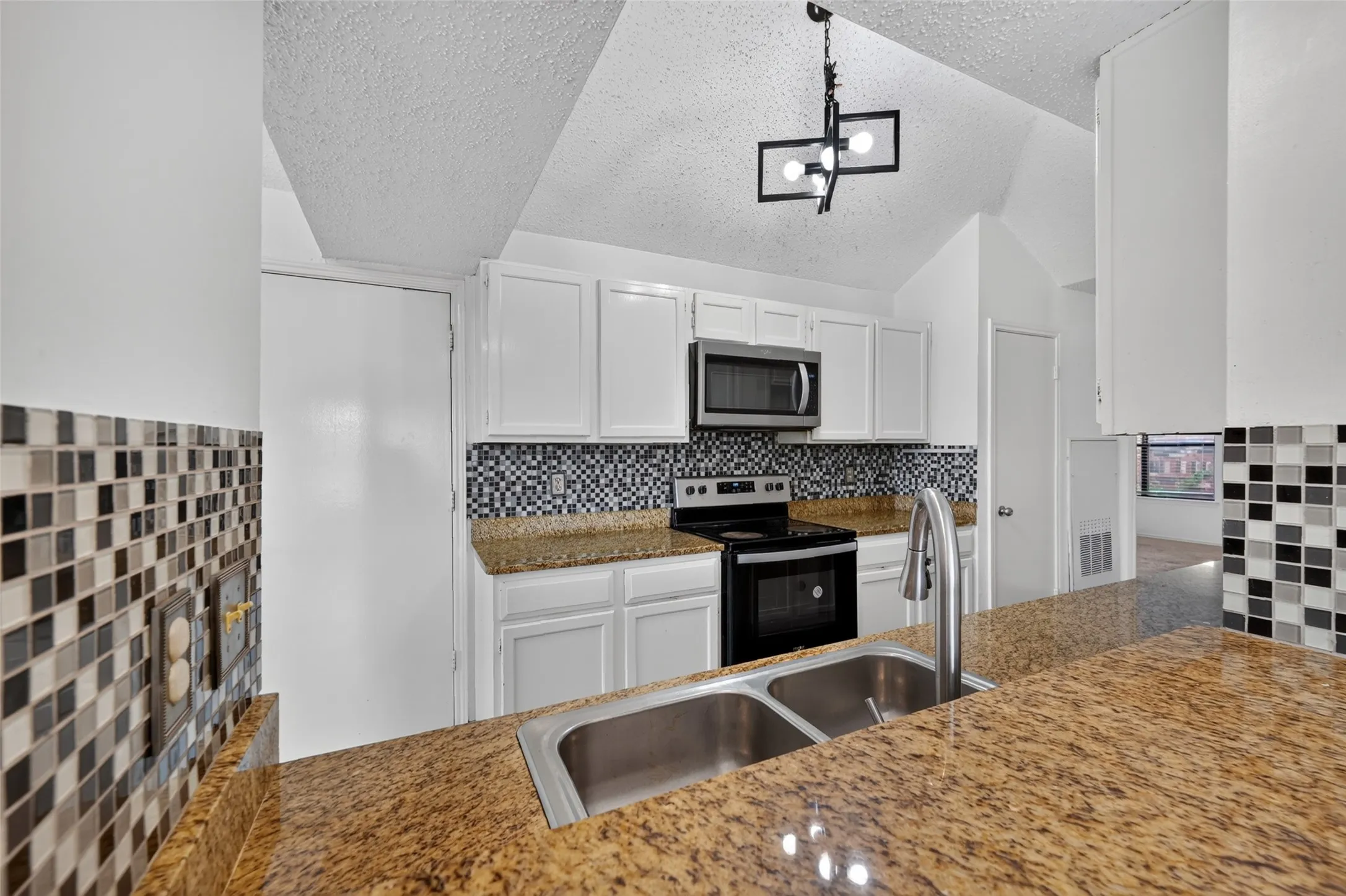 Granite countertops, stainless steel sink with gooseneck faucet, full suite of stainless steel appliances, white cabinetry, and multi-tone mosaic tile backsplash