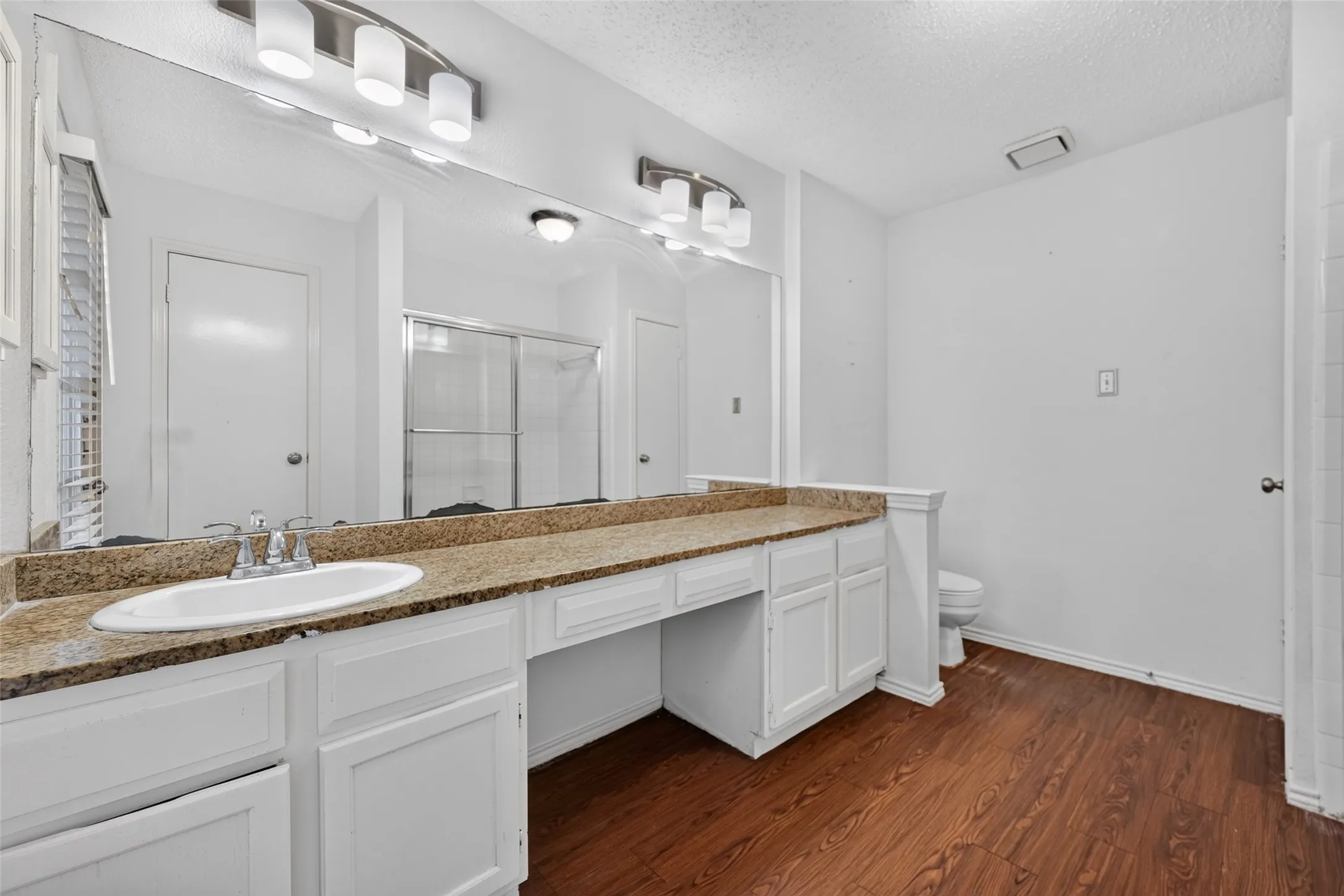 Dual vanity with a stone-finish countertop, white cabinetry, and wood-finish flooring