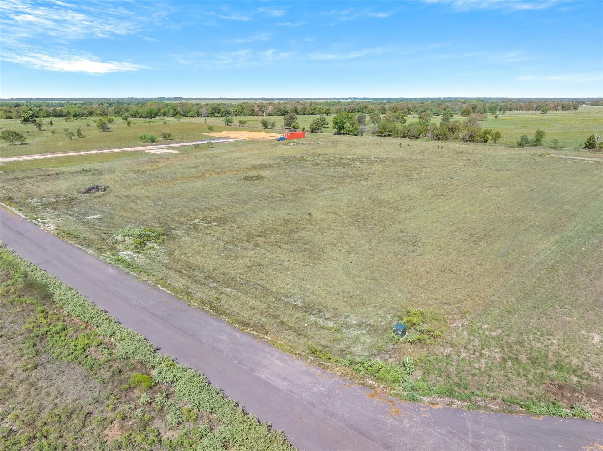 Expansive land parcel featuring a paved road, scattered trees, and a distant red structure