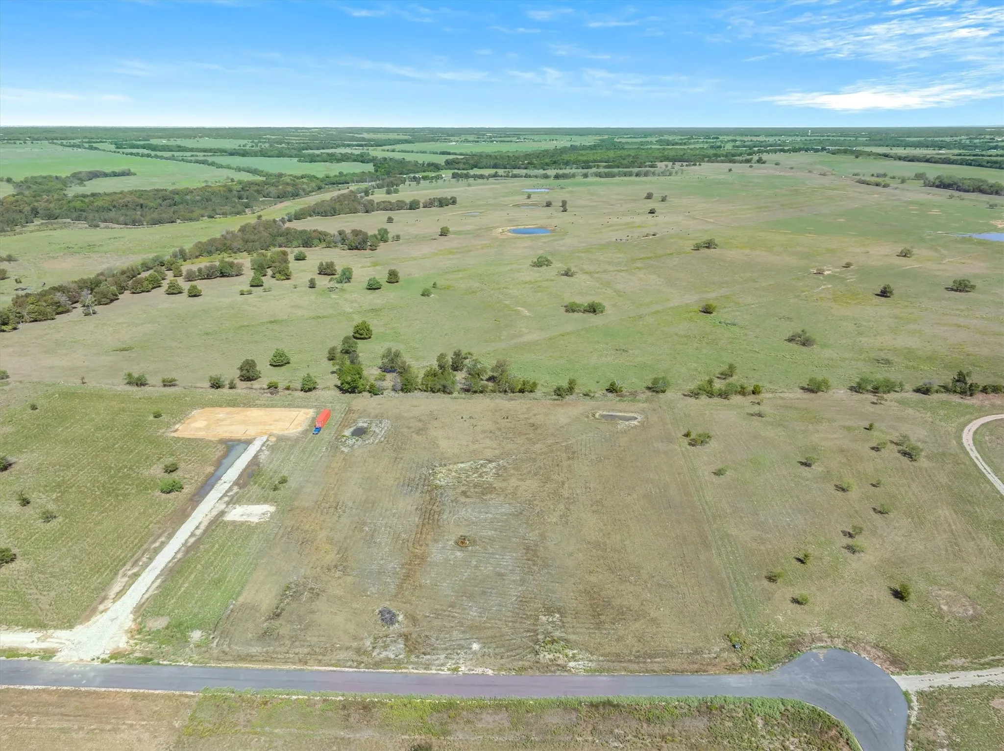 Expansive undeveloped land featuring a paved road, gravel drive, and scattered trees