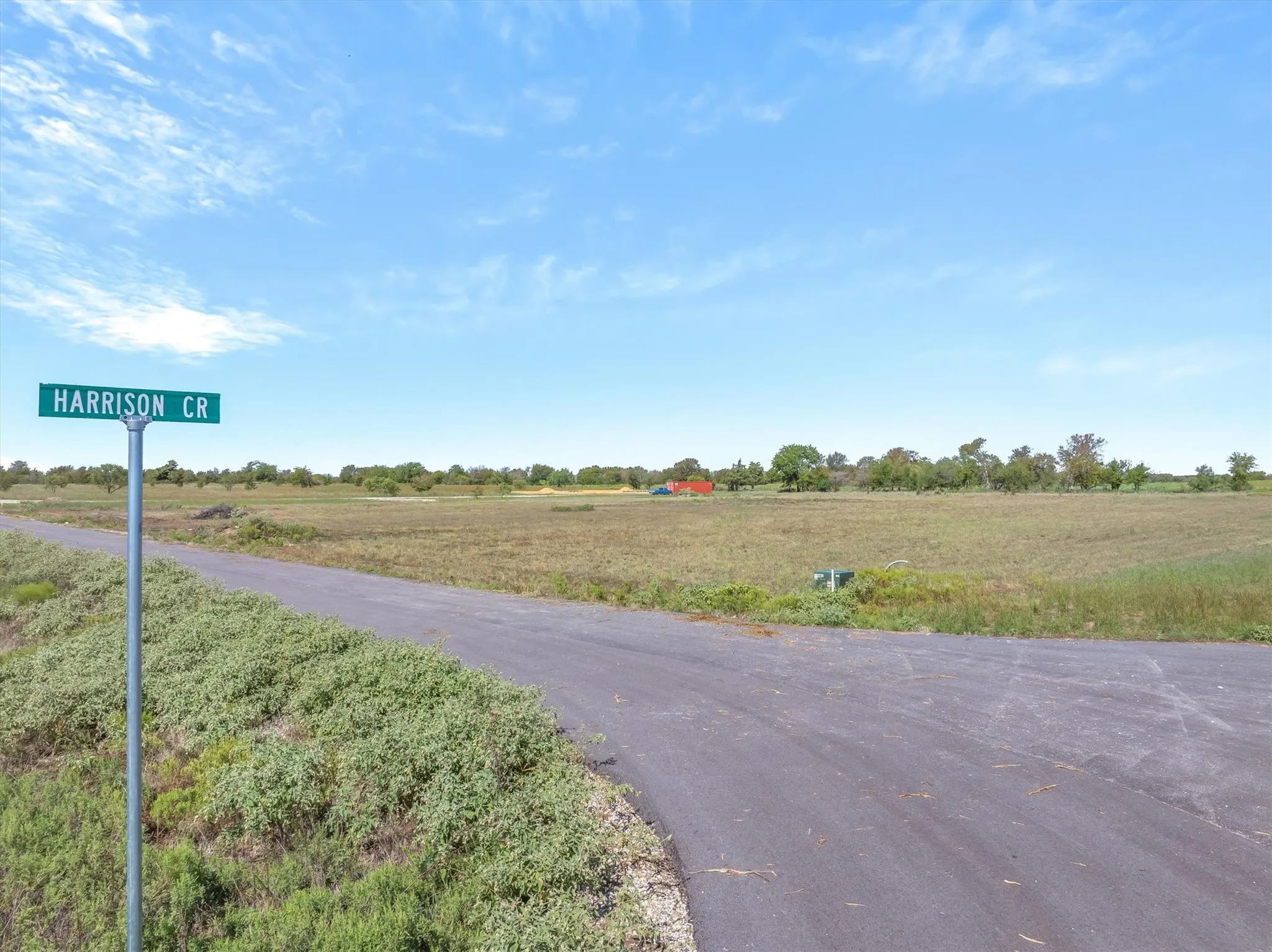 Rural acreage with a paved road, mature trees, and a clear blue sky overhead