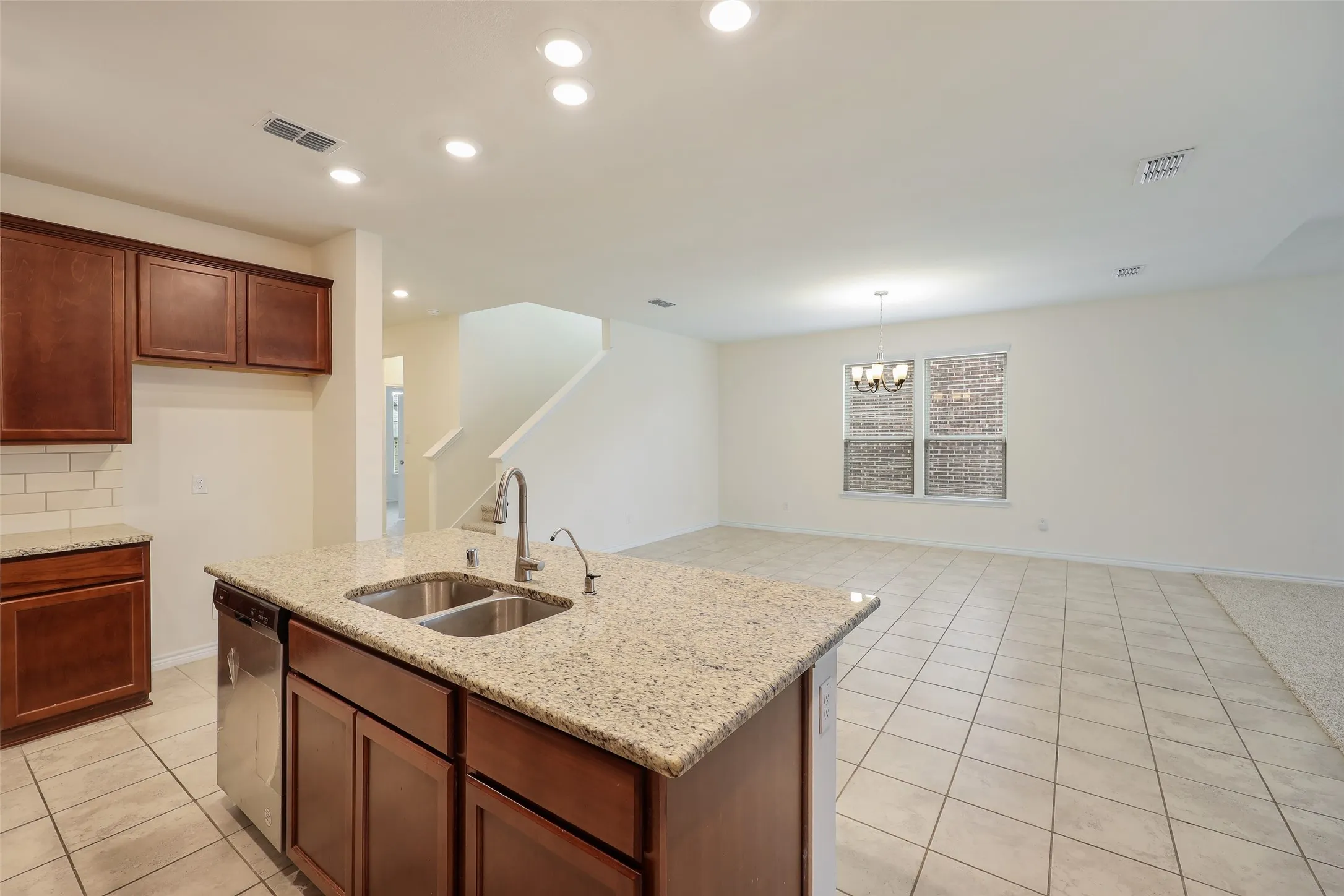 Kitchen featuring a central island with a dual-basin stainless steel sink, stone-finish countertops, recessed lighting, and tile flooring