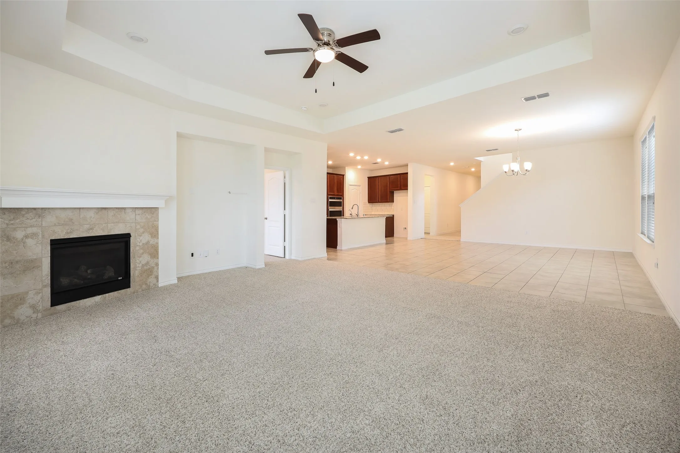 Tray ceiling featuring a central fan, tiled fireplace surround with a mantel, and neutral carpeting