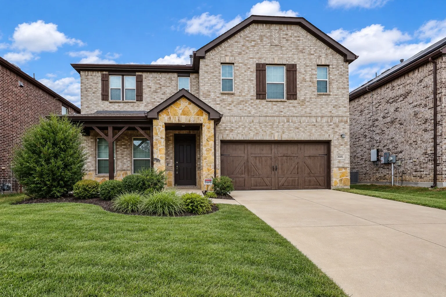 Virtually improved image. Two-story brick and stone veneer exterior featuring wood-finish decorative shutters, a covered entryway with timber-frame accents, and an attached multi-car garage with carriage-style doors
