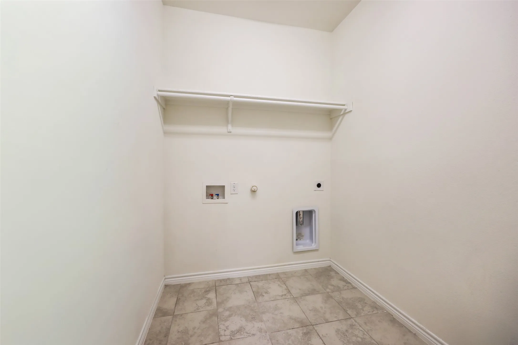 Utility area featuring neutral tile flooring, built-in overhead shelving, and dedicated hookups for laundry appliances