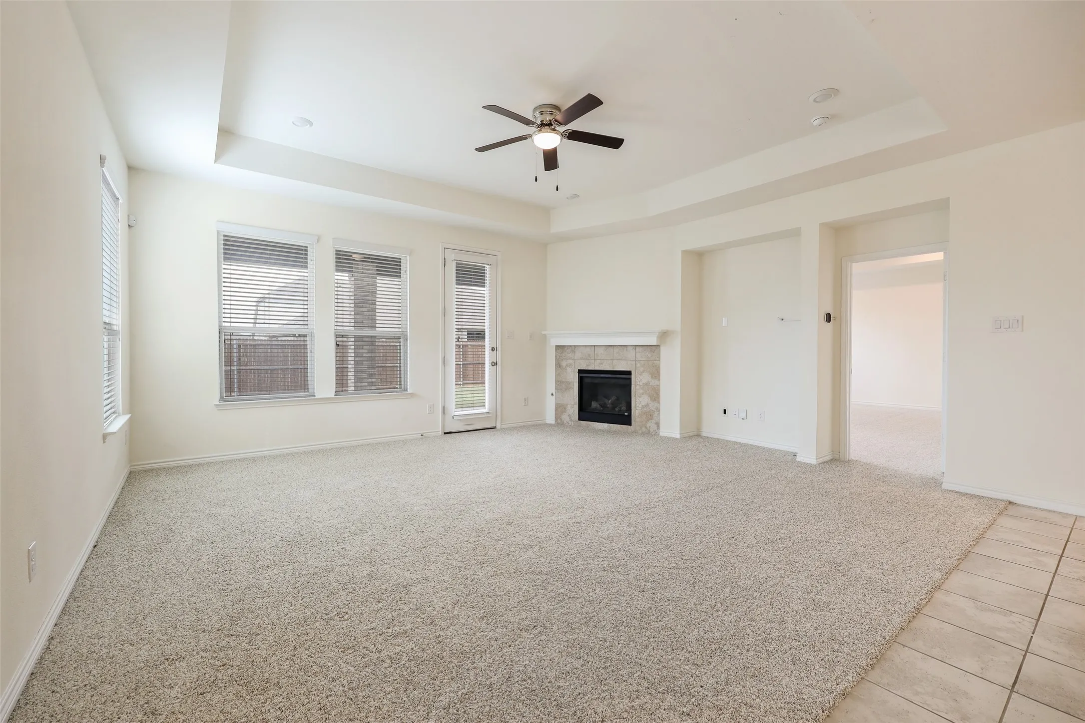 Living area featuring a tray ceiling, ceiling fan, carpeting, tiled fireplace surround, and access to exterior space