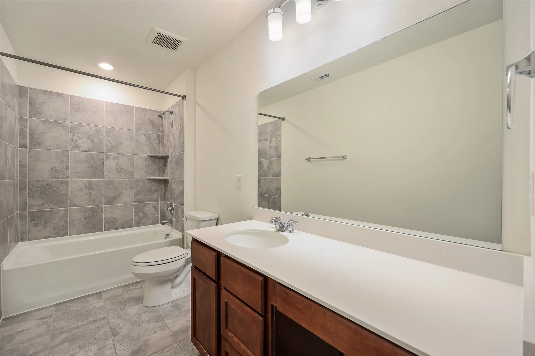 Bathroom featuring wood-finish cabinetry, a solid-surface vanity countertop, a large wall-mounted mirror, and tile-surround bathtub