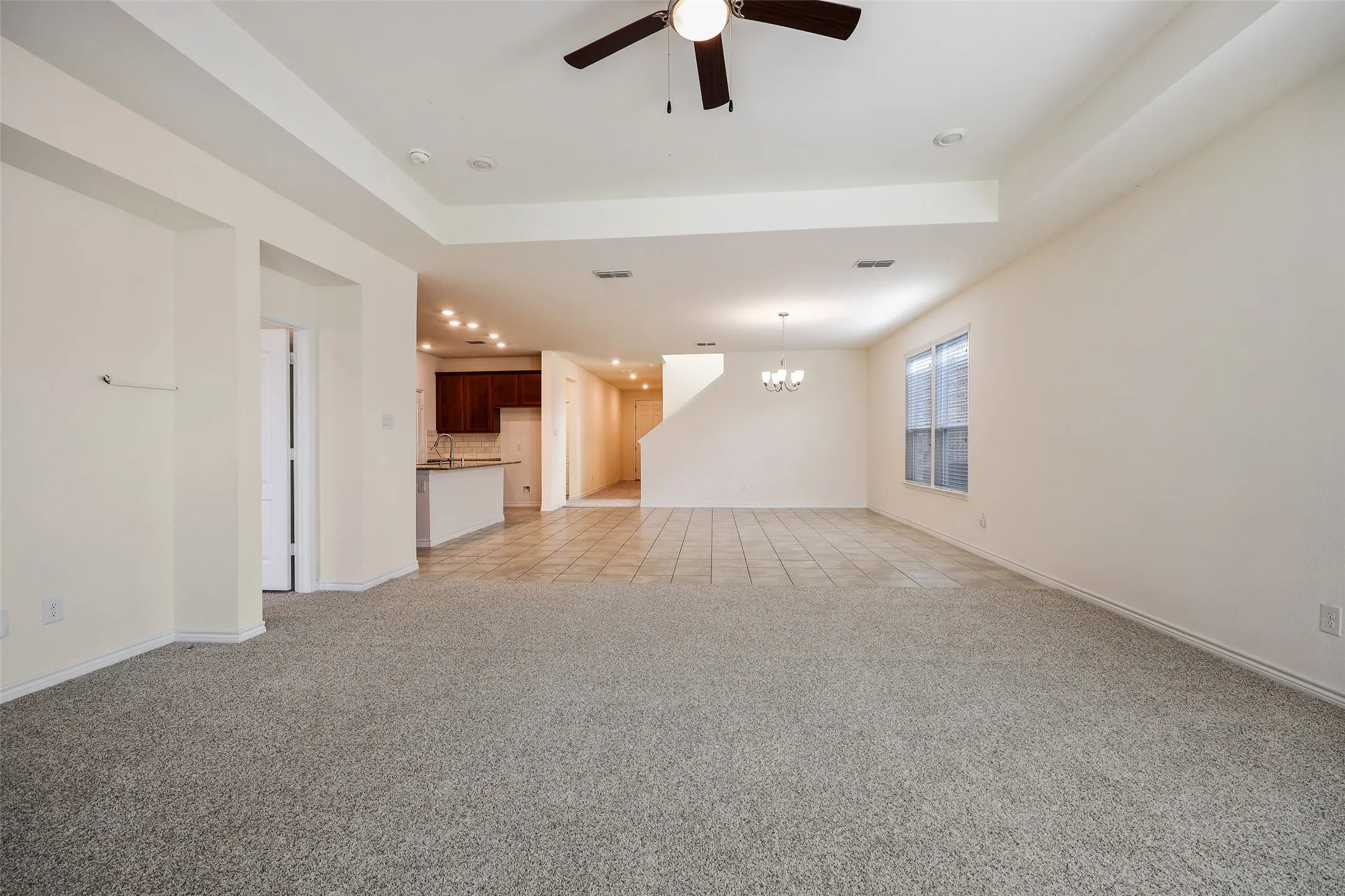 Tray ceiling featuring a central lighted ceiling fan, neutral wall-to-wall carpeting, large format tile flooring, recessed lighting, and kitchen cabinetry with a peninsula