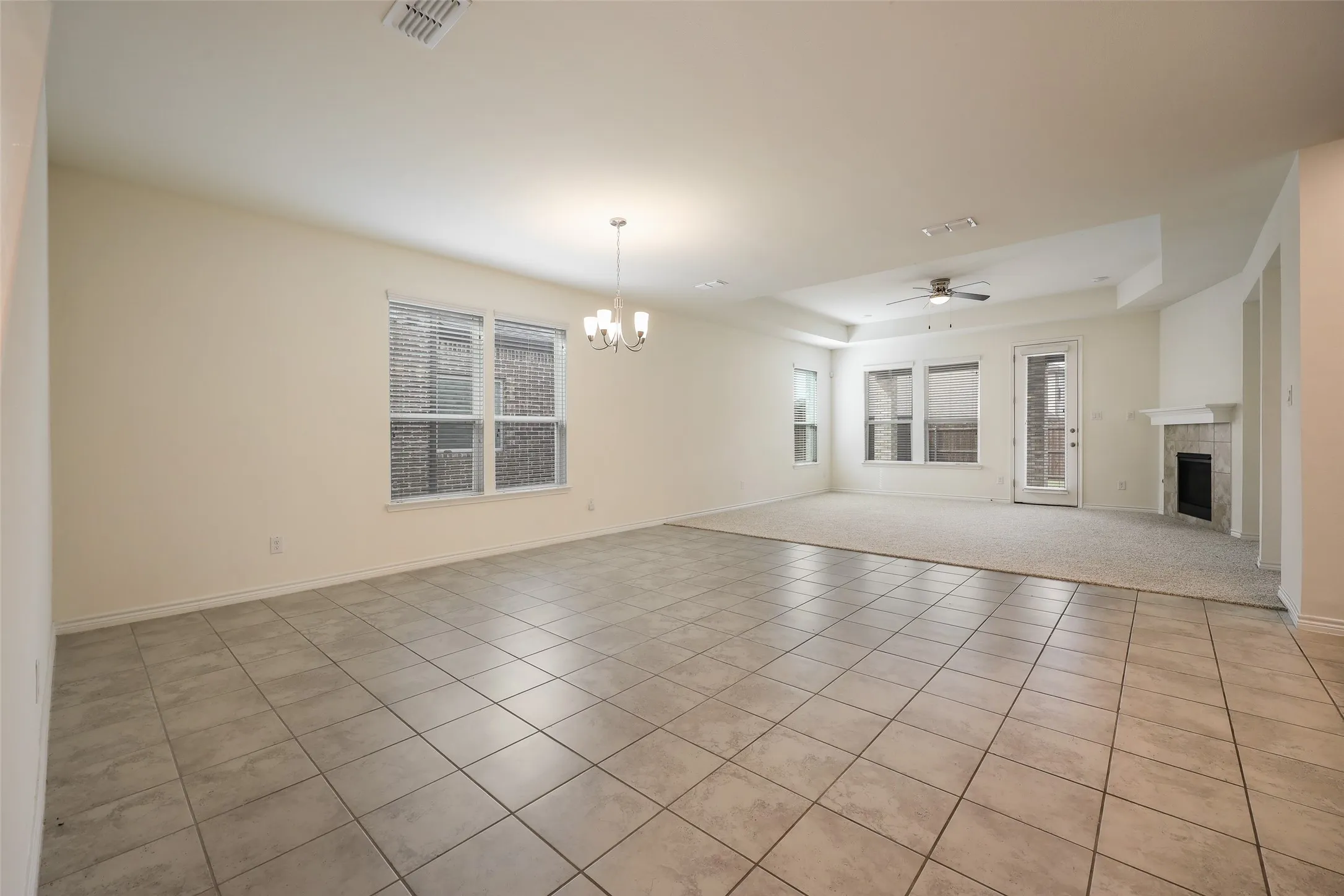 Open-concept interior featuring large-format ceramic tile flooring, a multi-light chandelier, a recessed tray ceiling with a center fan, and a fireplace with a stone-surround mantel