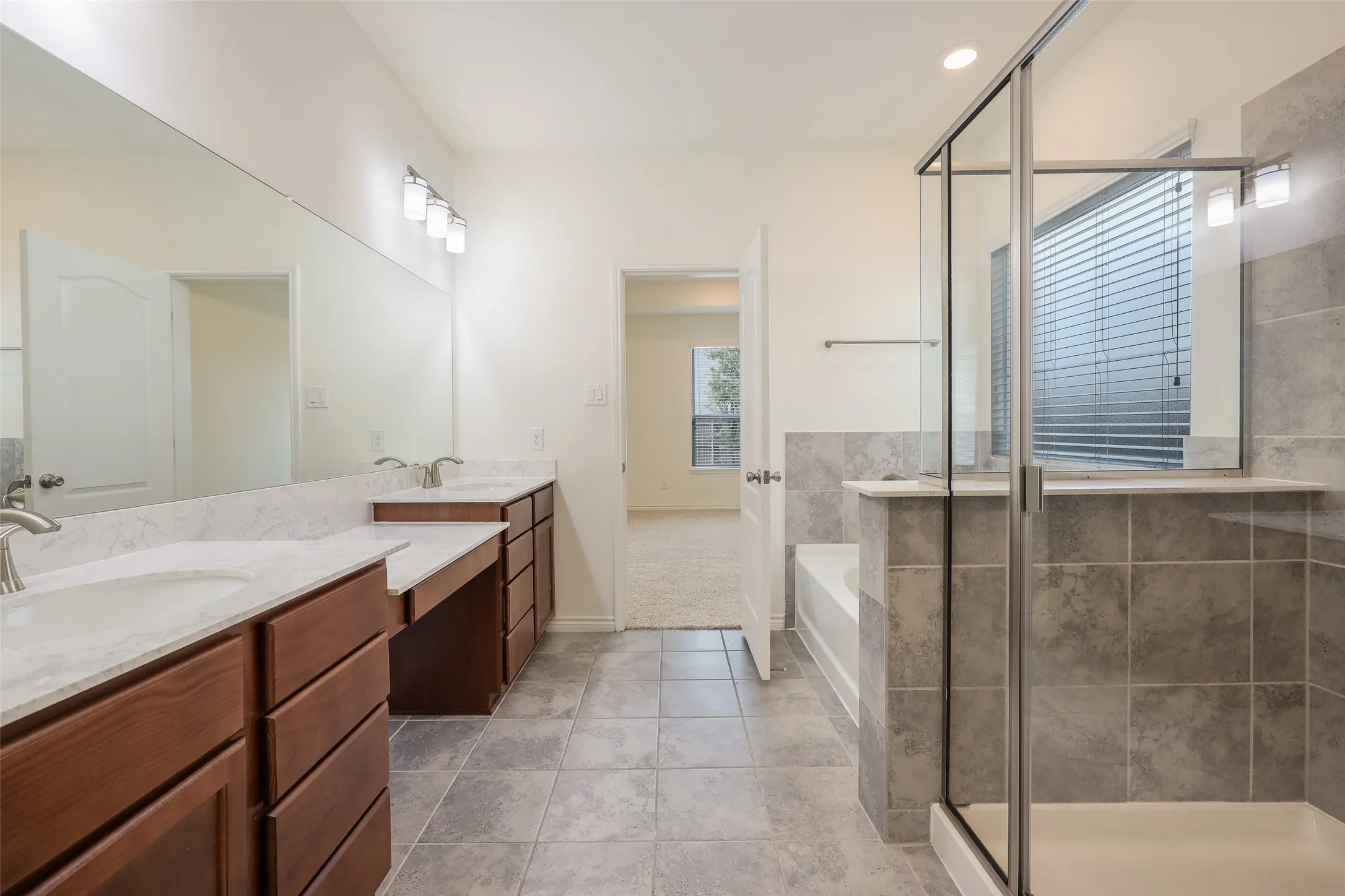 Dual vanity with solid-surface countertops, wood-finish cabinetry, tile flooring, and a glass-enclosed shower with tile surround