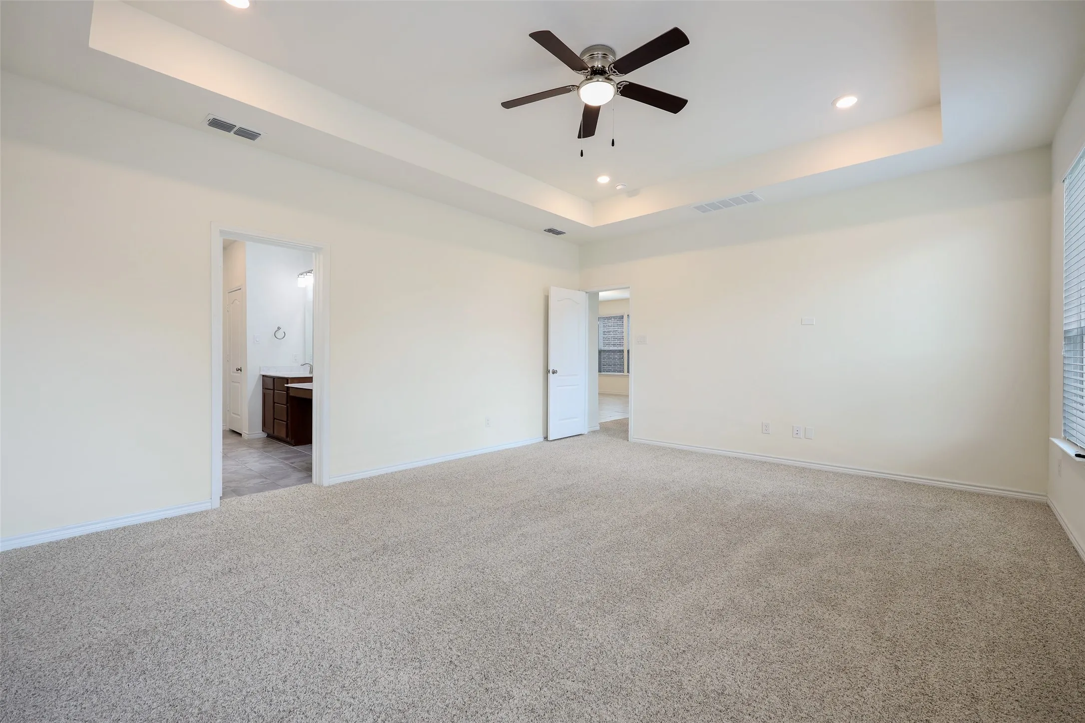 Spacious room featuring a tray ceiling, neutral wall-to-wall carpeting, and a ceiling fan with integrated lighting