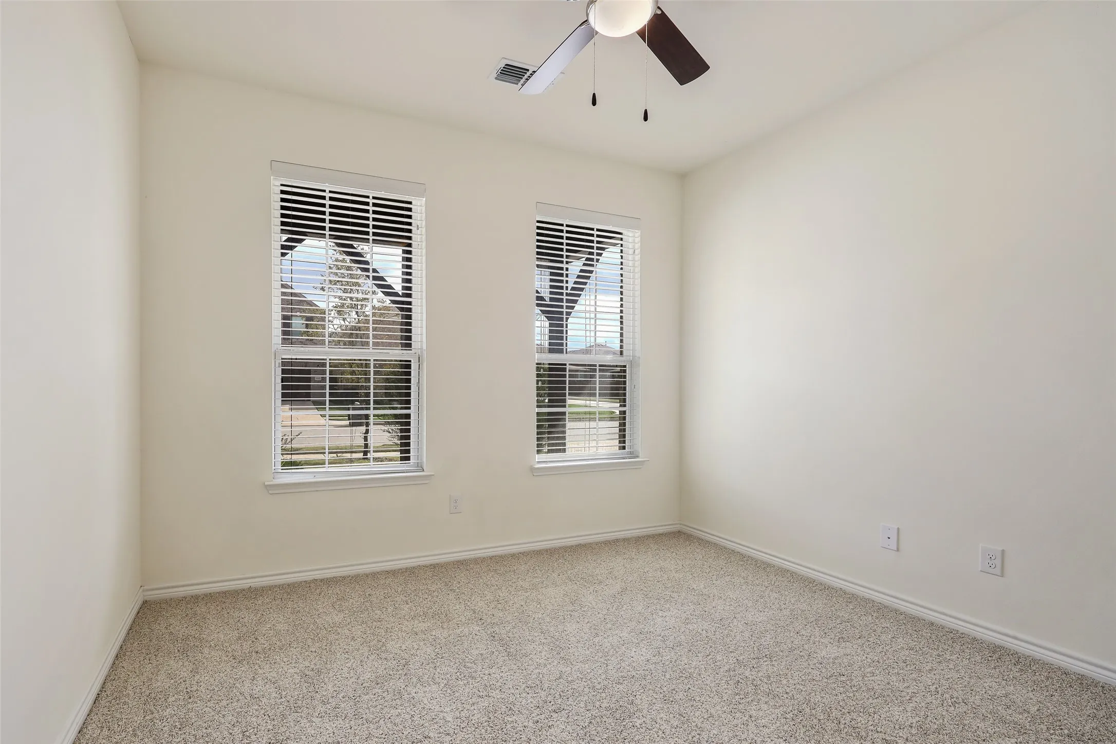 Neutral wall-to-wall carpeting, two dual-pane windows with horizontal blinds, and a ceiling fan with integrated lighting fixture