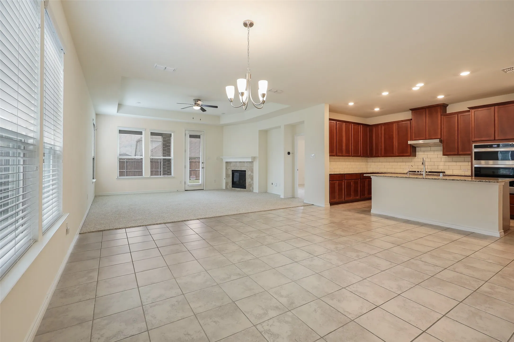 Open-concept area featuring ceramic tile flooring, built-in fireplace, tray ceiling, kitchen with dark wood cabinetry, and recessed lighting