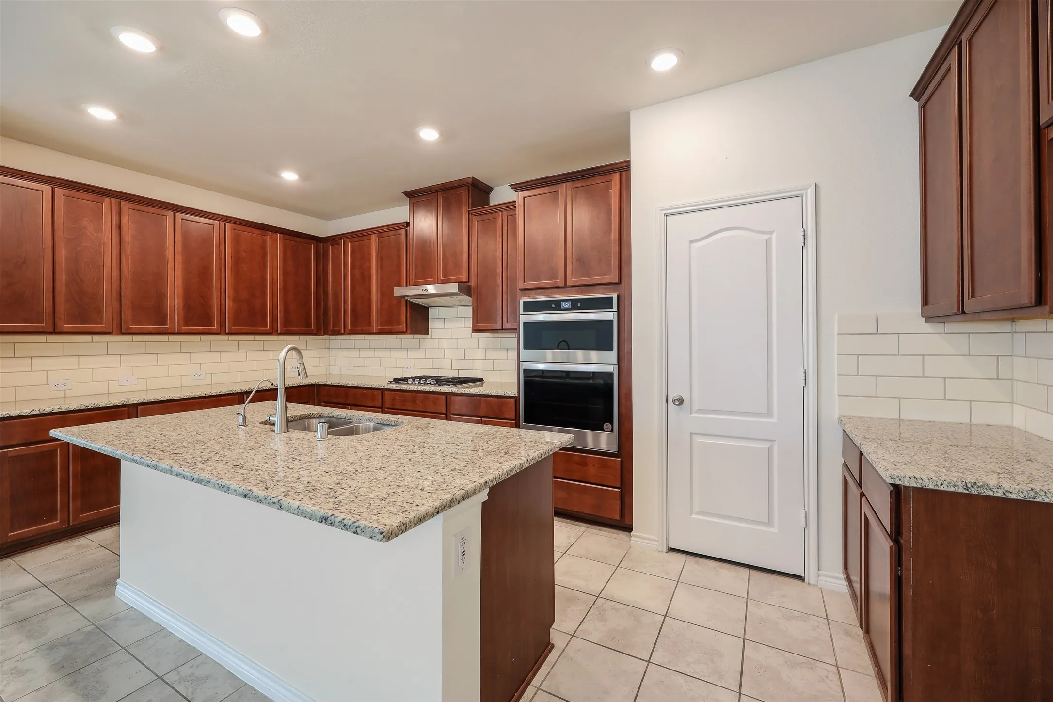 Kitchen featuring cherry-tone cabinetry, stone-surface countertops, subway tile backsplash, stainless steel built-in double wall ovens, and recessed lighting
