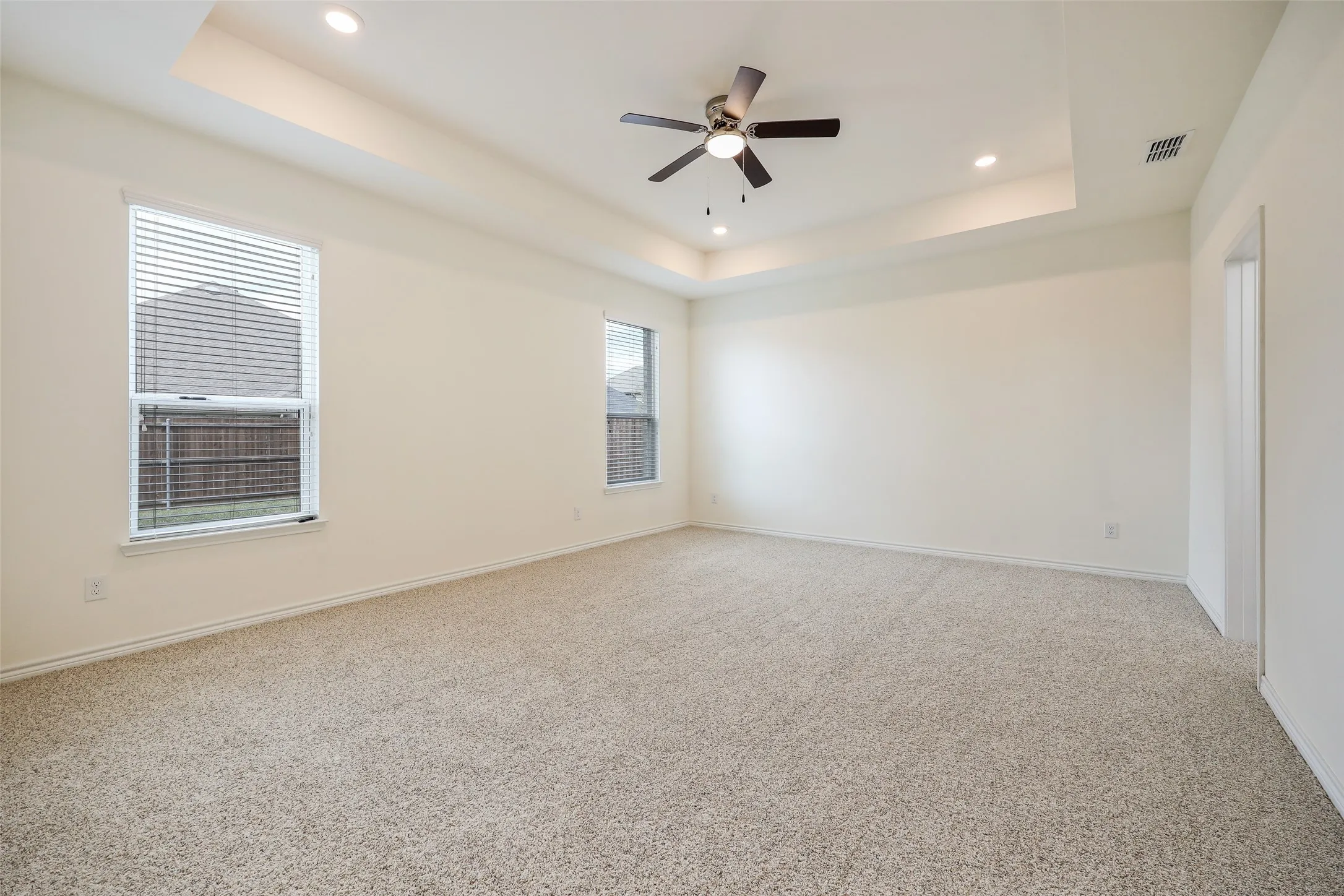Interior room featuring a tray ceiling, recessed lighting, a ceiling fan, neutral carpeting, and multi-pane windows
