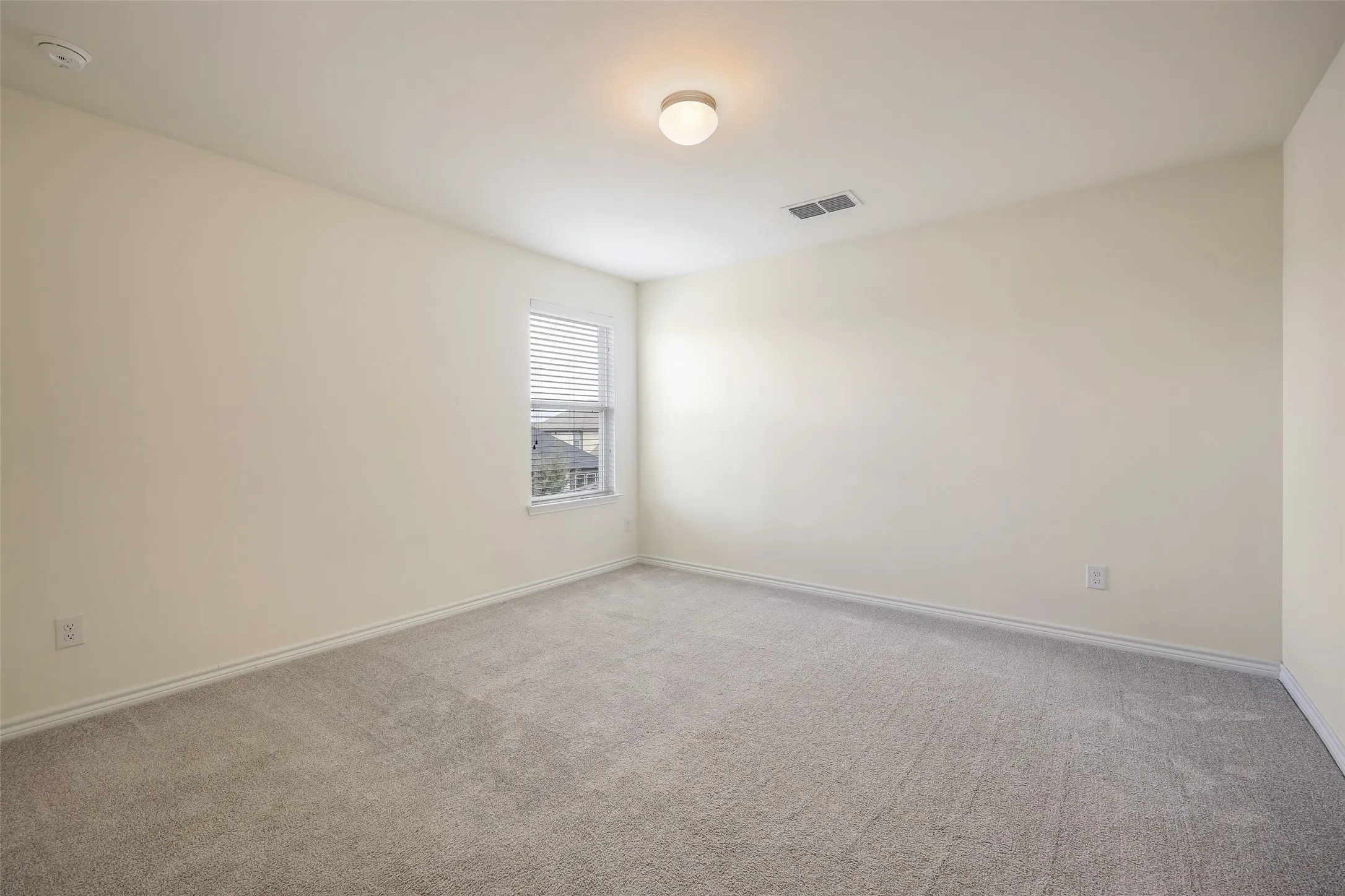 Neutral-toned room featuring neutral carpeting, a single window with blinds, and a central flush-mount ceiling light fixture