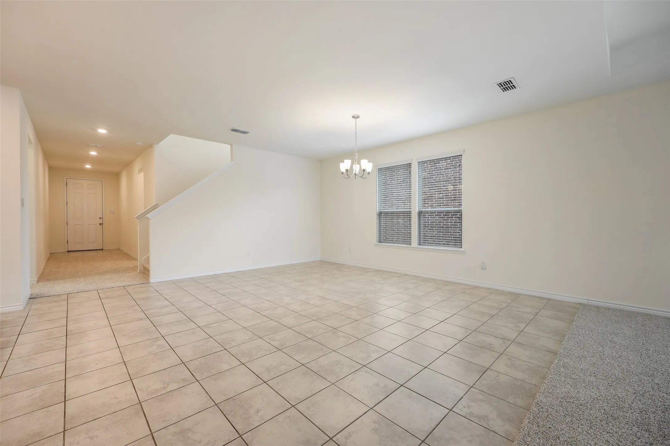 Open-concept interior featuring neutral wall tones, large-format ceramic tile flooring, a multi-arm chandelier, and double-paned windows