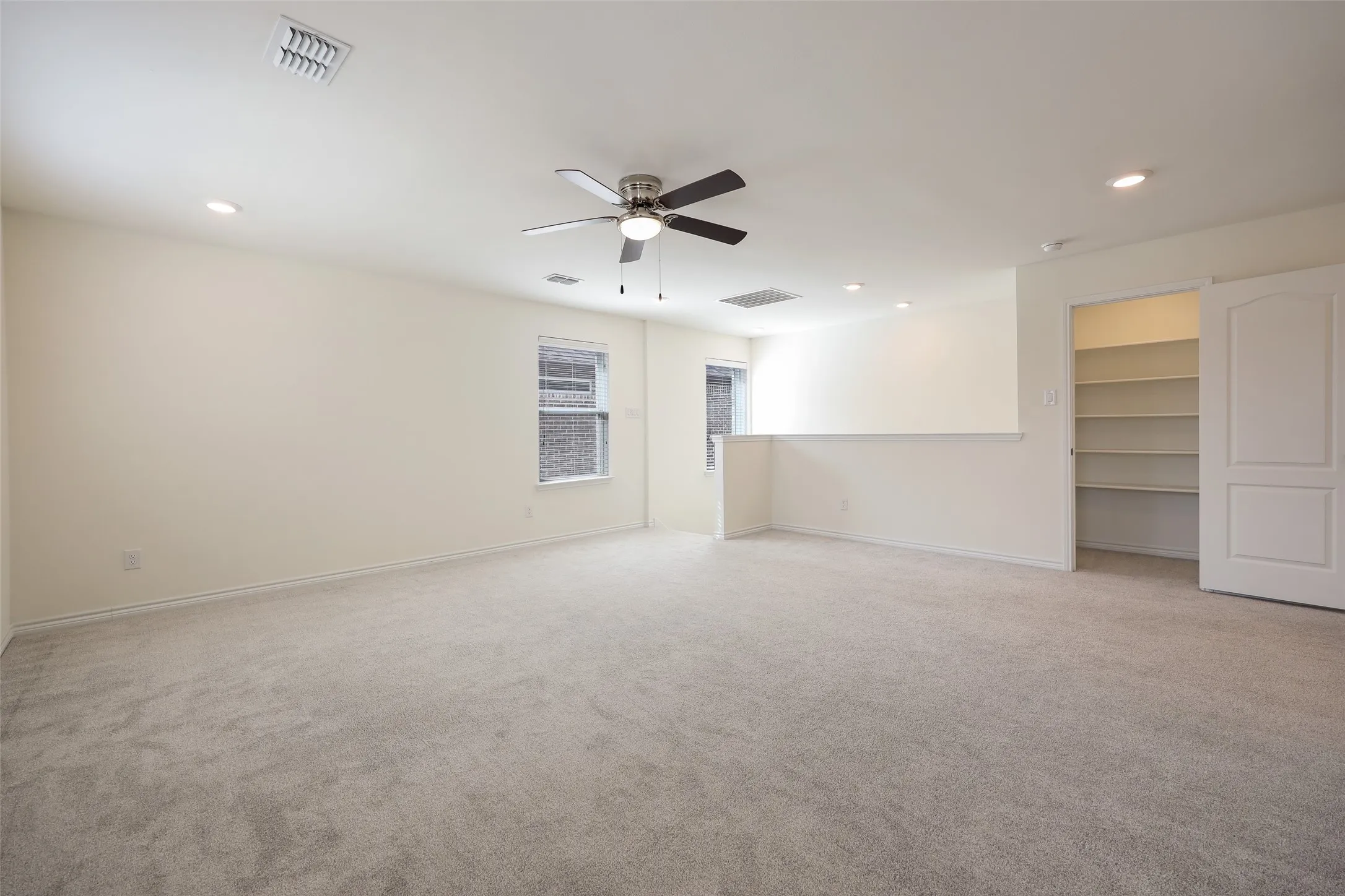 Neutral-toned interior space featuring carpeted flooring, a ceiling fan with integrated lighting, recessed lighting, and a built-in walk-in storage area with shelving