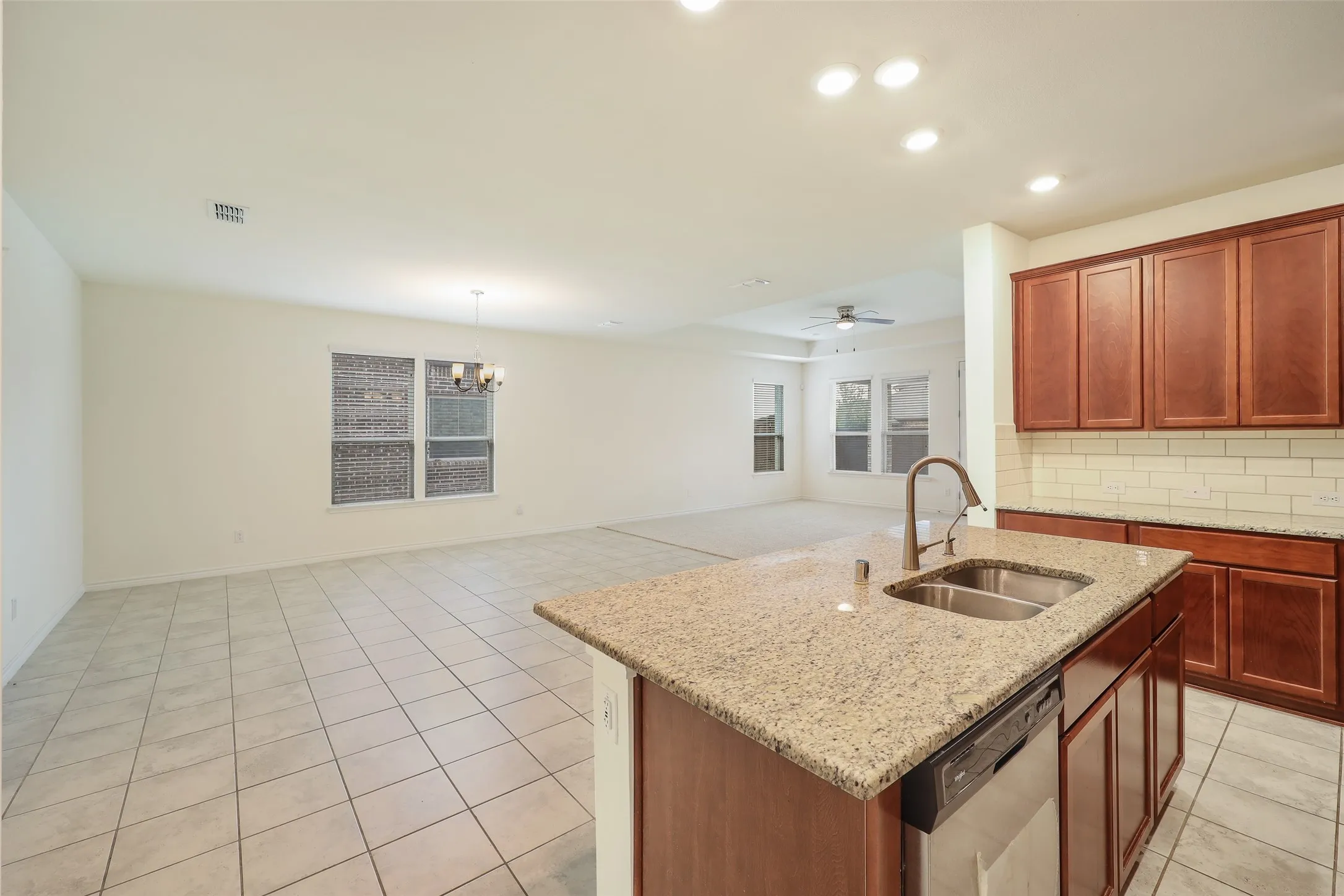 Kitchen featuring a center island, stone-finish countertops, stainless steel dual-basin sink, tile backsplash, and wood cabinetry