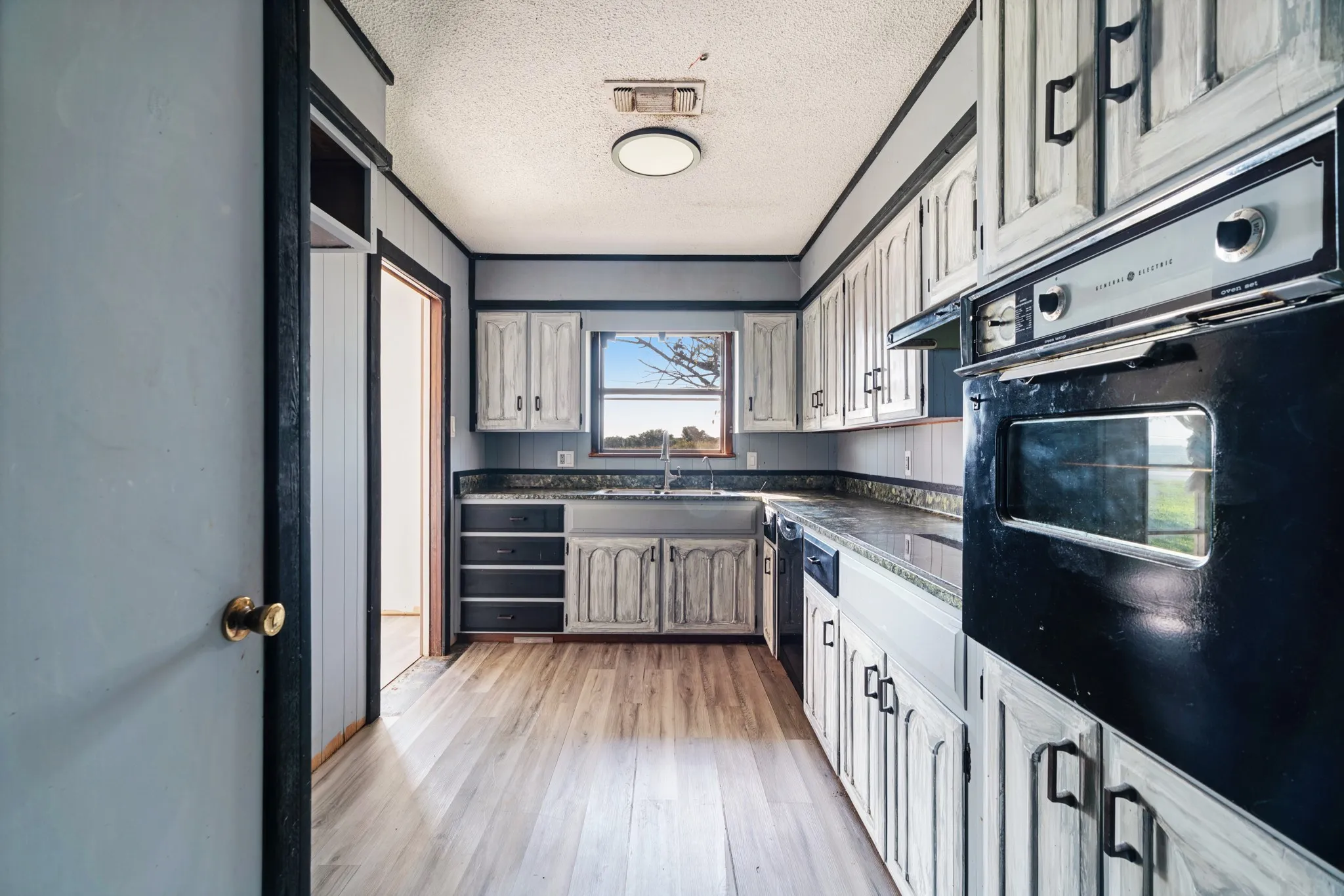 Kitchen with black appliances, a textured ceiling, light wood-type flooring, and dark countertops