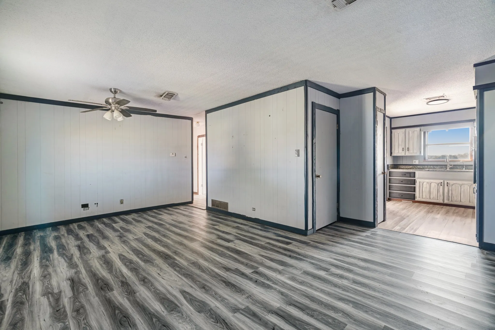 Unfurnished living room featuring dark wood-type flooring, a textured ceiling, wood walls, crown molding, and ceiling fan