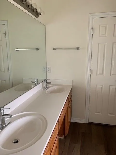Double vanity featuring a solid surface countertop, integrated dual basins, polished chrome faucets, a full-width wall mirror, and wood-finish flooring