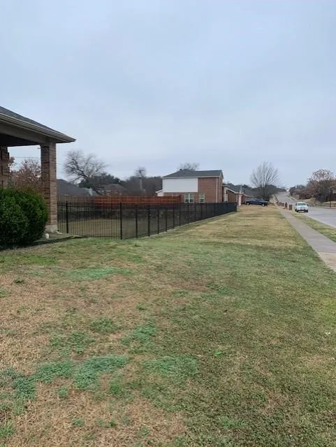 Exterior space featuring a brick-columned covered porch, black metal perimeter fencing, and a wood-slat privacy screen