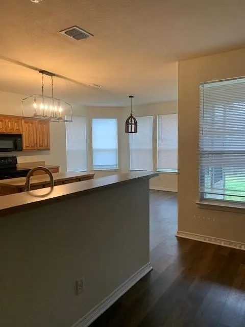 Kitchen featuring wood cabinetry, a breakfast bar, wood-finish flooring, a rectangular metal-frame pendant light, and a bay window