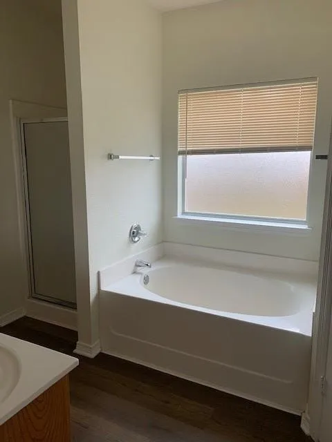Bathroom featuring a soaking tub, separate shower enclosure with a glass door, and wood-finish flooring