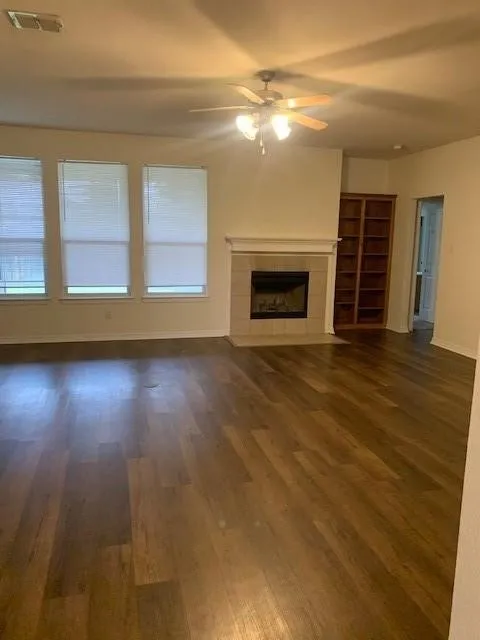 Wood-finish flooring, masonry fireplace with a classic mantel, built-in wooden shelving, and ceiling fan with integrated​​‌​​​​‌​​‌‌​‌‌​​​‌‌​‌​‌​‌​​​‌​​ lighting
