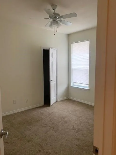 Interior space featuring neutral wall tones, wall-to-wall carpeting, a multi-blade ceiling fan with integrated lighting, and a six-panel interior door