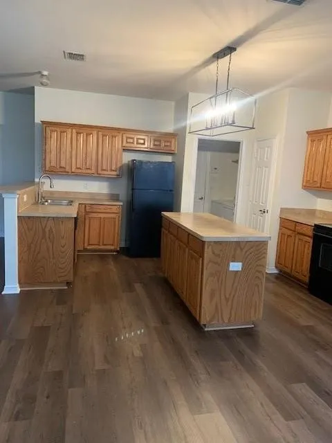 Kitchen featuring wood cabinetry, laminate countertops, a center island, wood-finish flooring, and a modern rectangular pendant light fixture